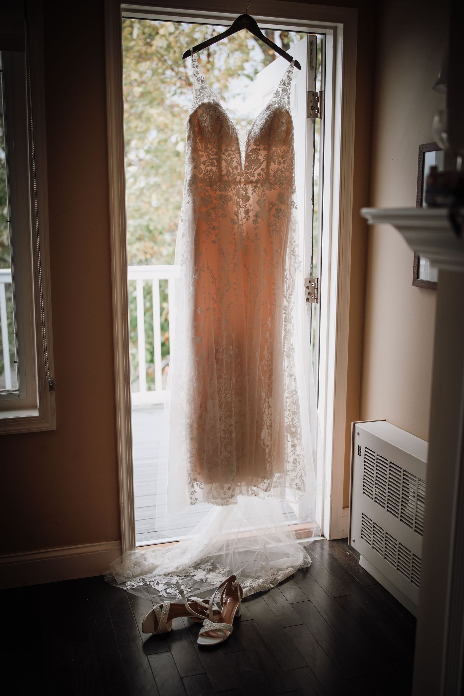 A wedding dress hangs in front of a window, creating an ethereal silhouette in natural light.