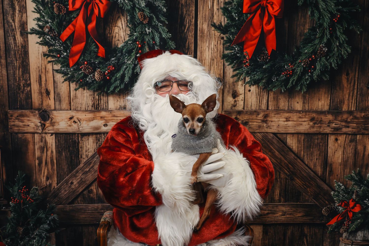 Festive holiday scene with wreaths and red bows against barn wood paneling.