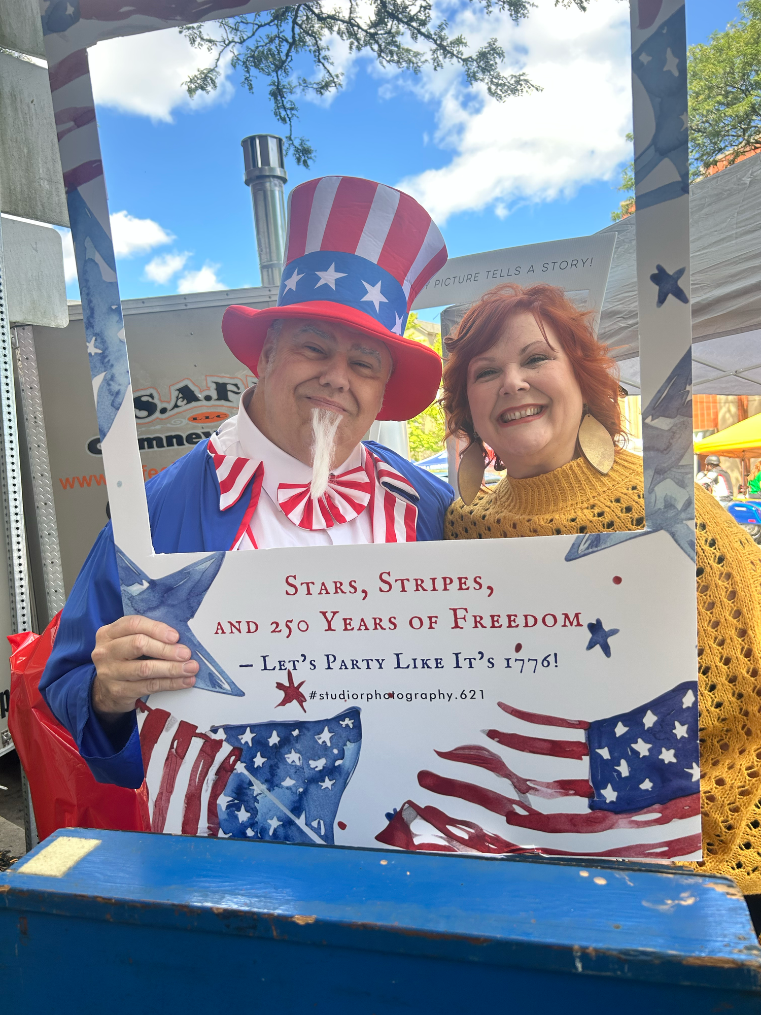 Attendees in patriotic attire hold signs at an outdoor freedom celebration event under blue skies.
