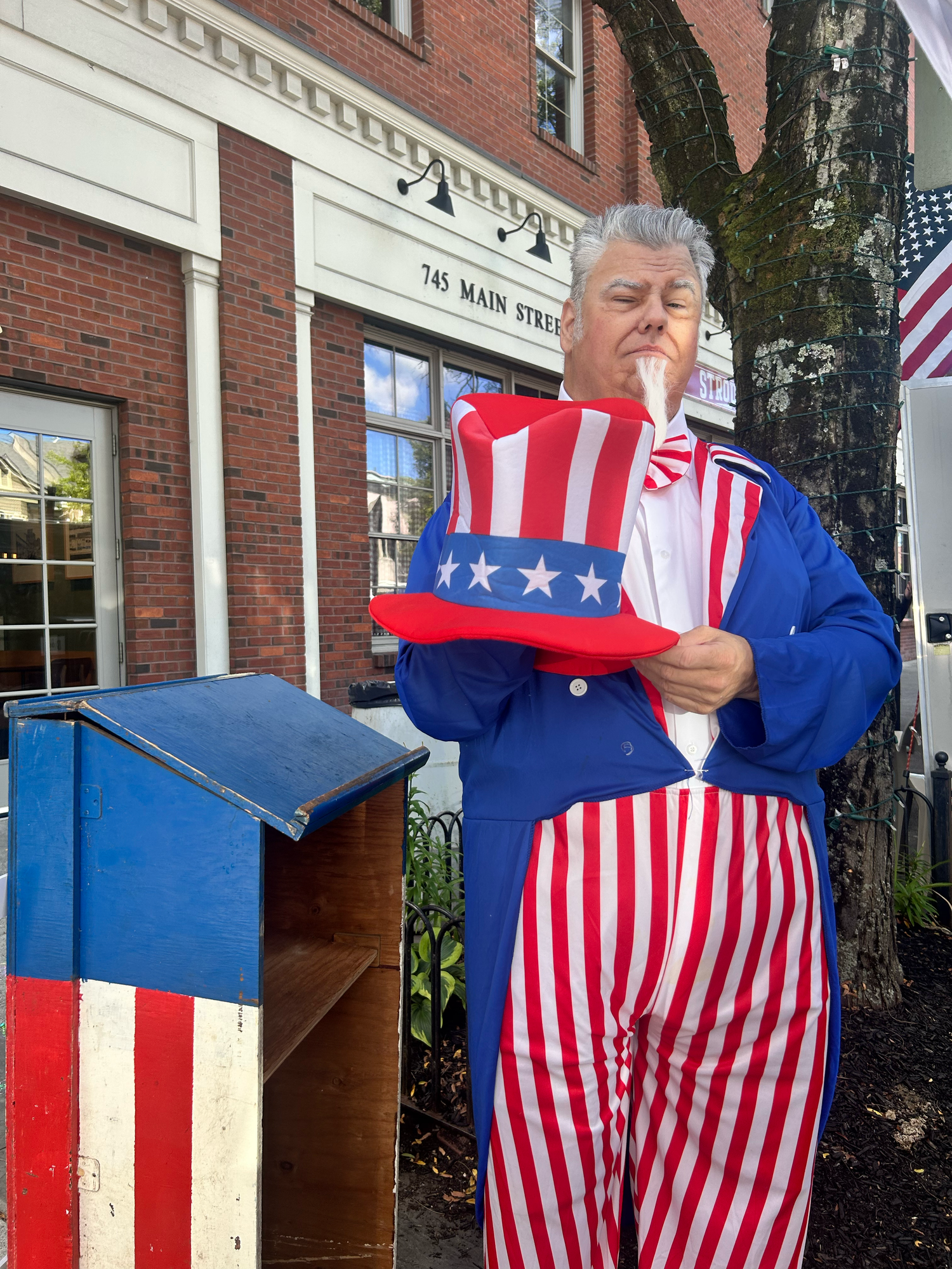 Patriotic red white and blue Uncle Sam figures displayed in front of a brick storefront with American flags.