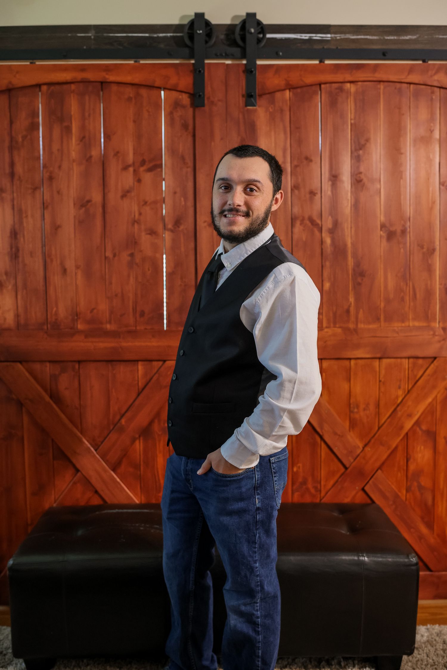 A person in a black vest and white shirt poses in front of a wooden barn door in a progressive sequence of photos.