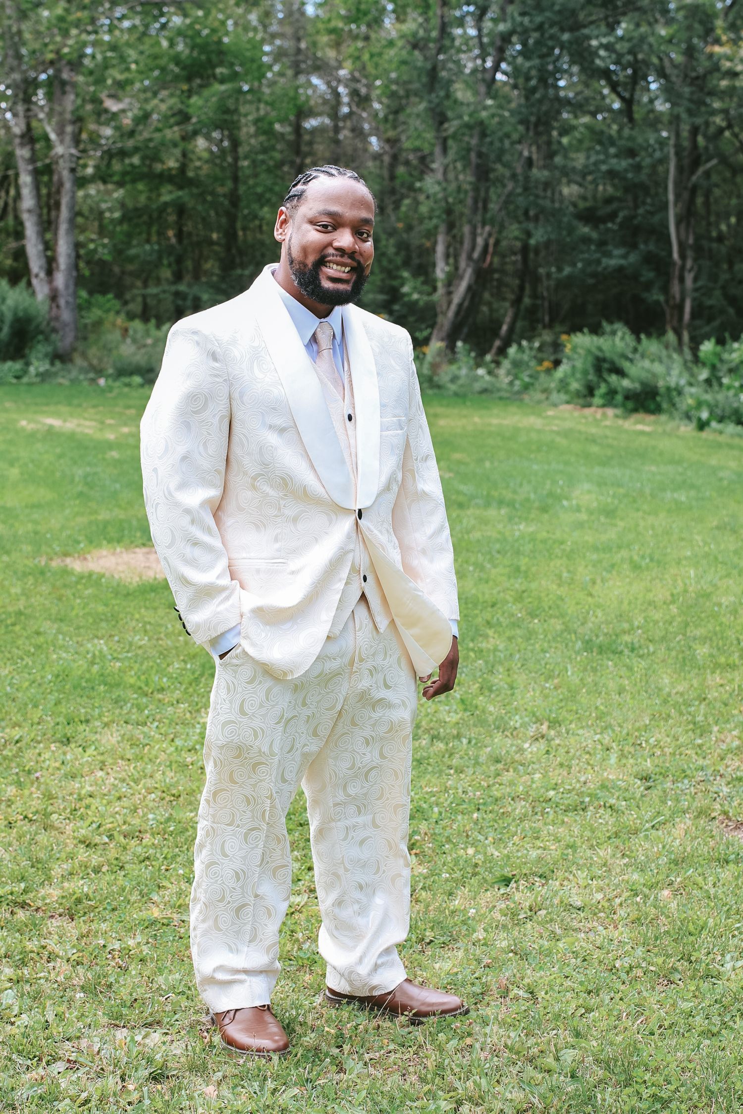 A person in a crisp white suit stands on lush green grass with trees in the background.