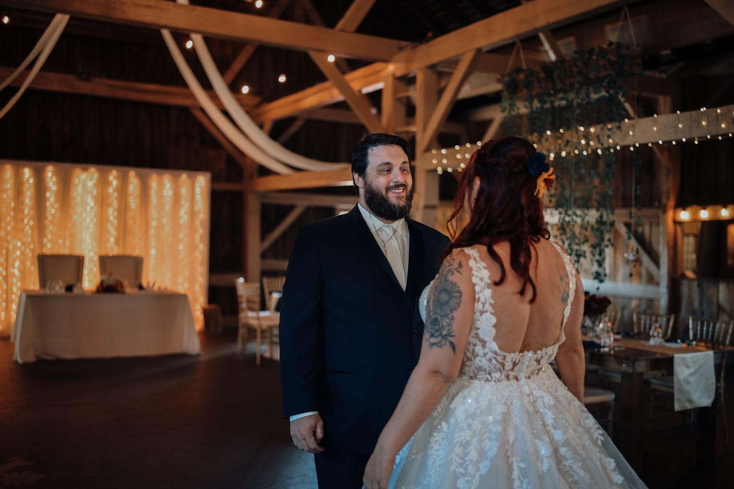 A couple shares their first dance at a rustic barn wedding reception under twinkling lights and wooden beams.