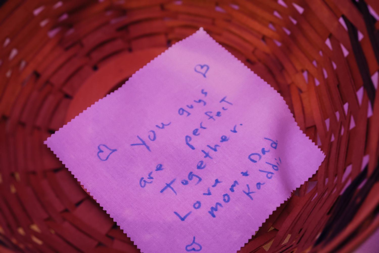 A pink handwritten note sits inside a red woven basket, captured in soft focus.