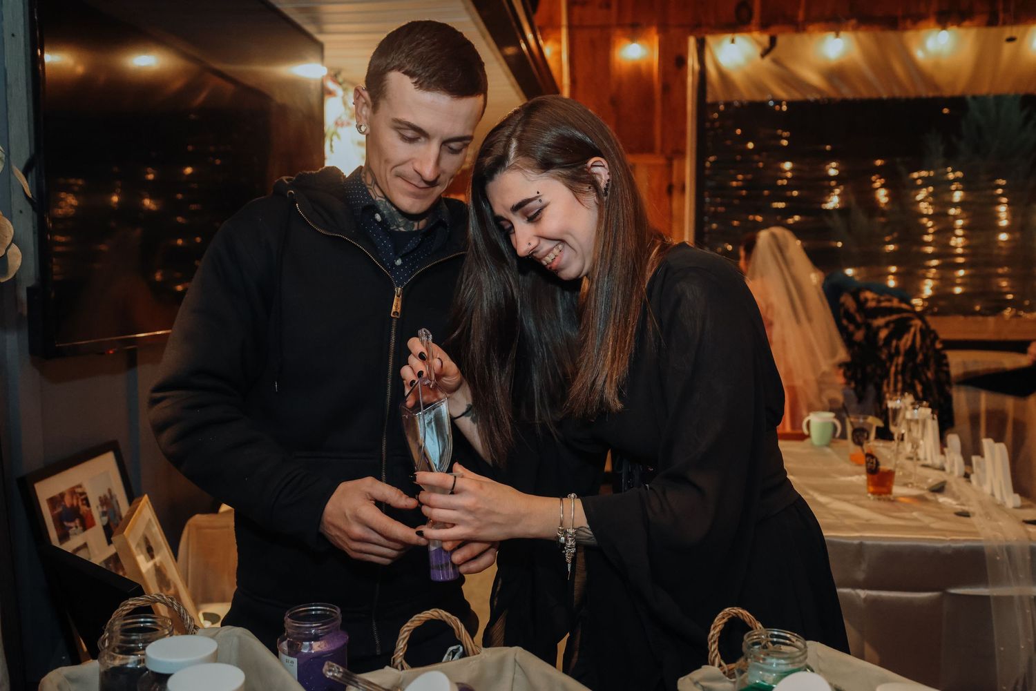 A couple in black attire shares an intimate moment while dining at a cozy restaurant with ambient lighting.