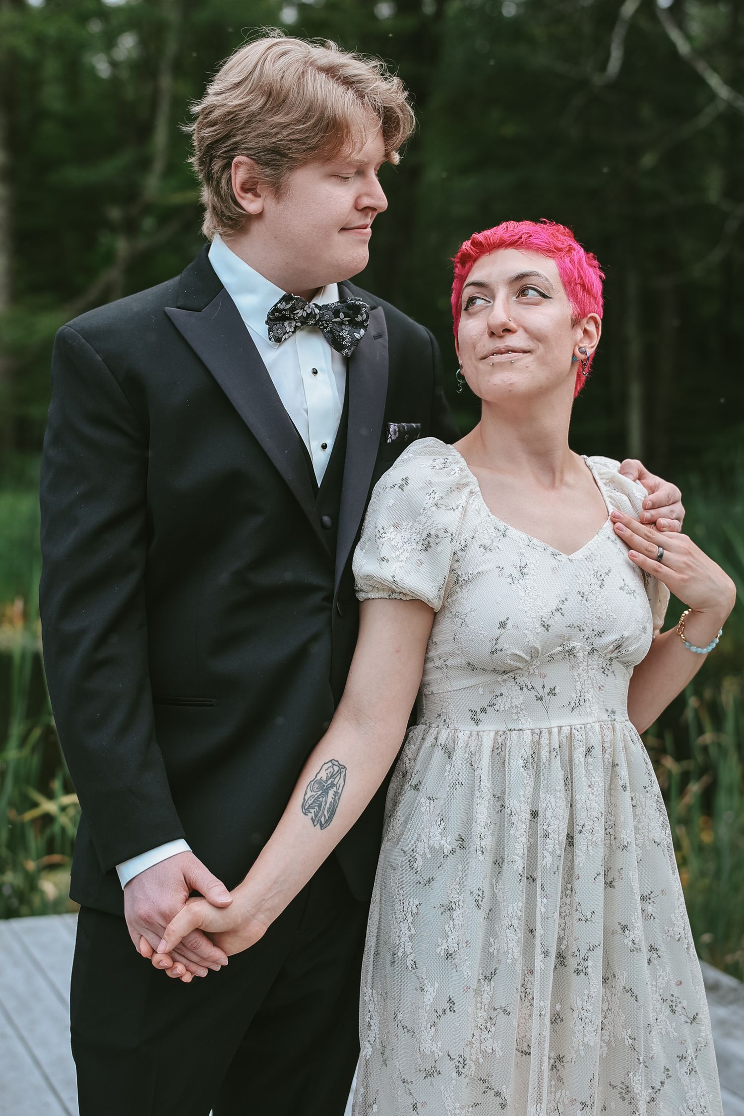 A couple in formal wedding attire holds hands while walking outdoors, with the bride wearing a floral empire waist dress.