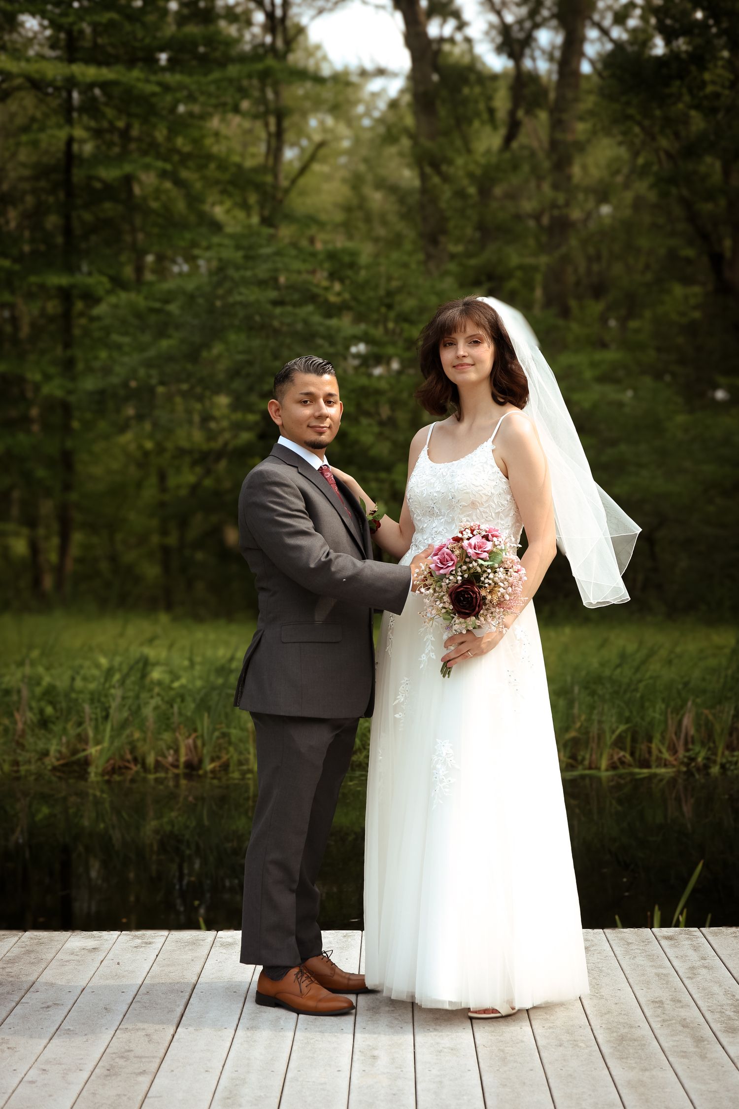 A couple stands together on a wooden deck surrounded by lush greenery during their outdoor wedding ceremony.