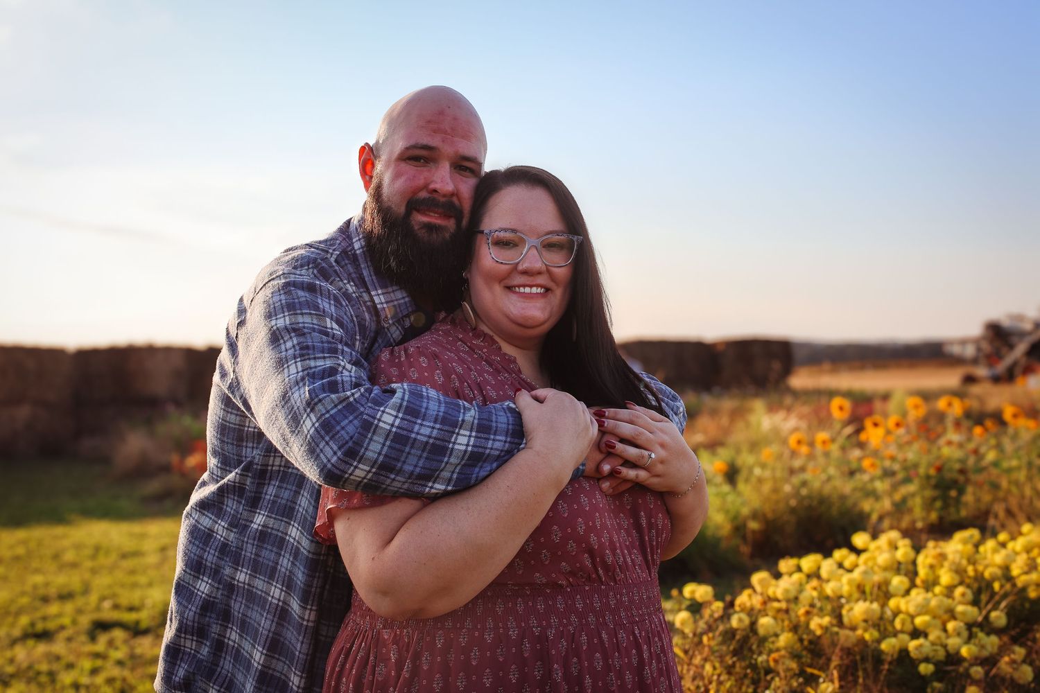 A couple embraces in a golden field of wildflowers during sunset, creating a romantic outdoor portrait.