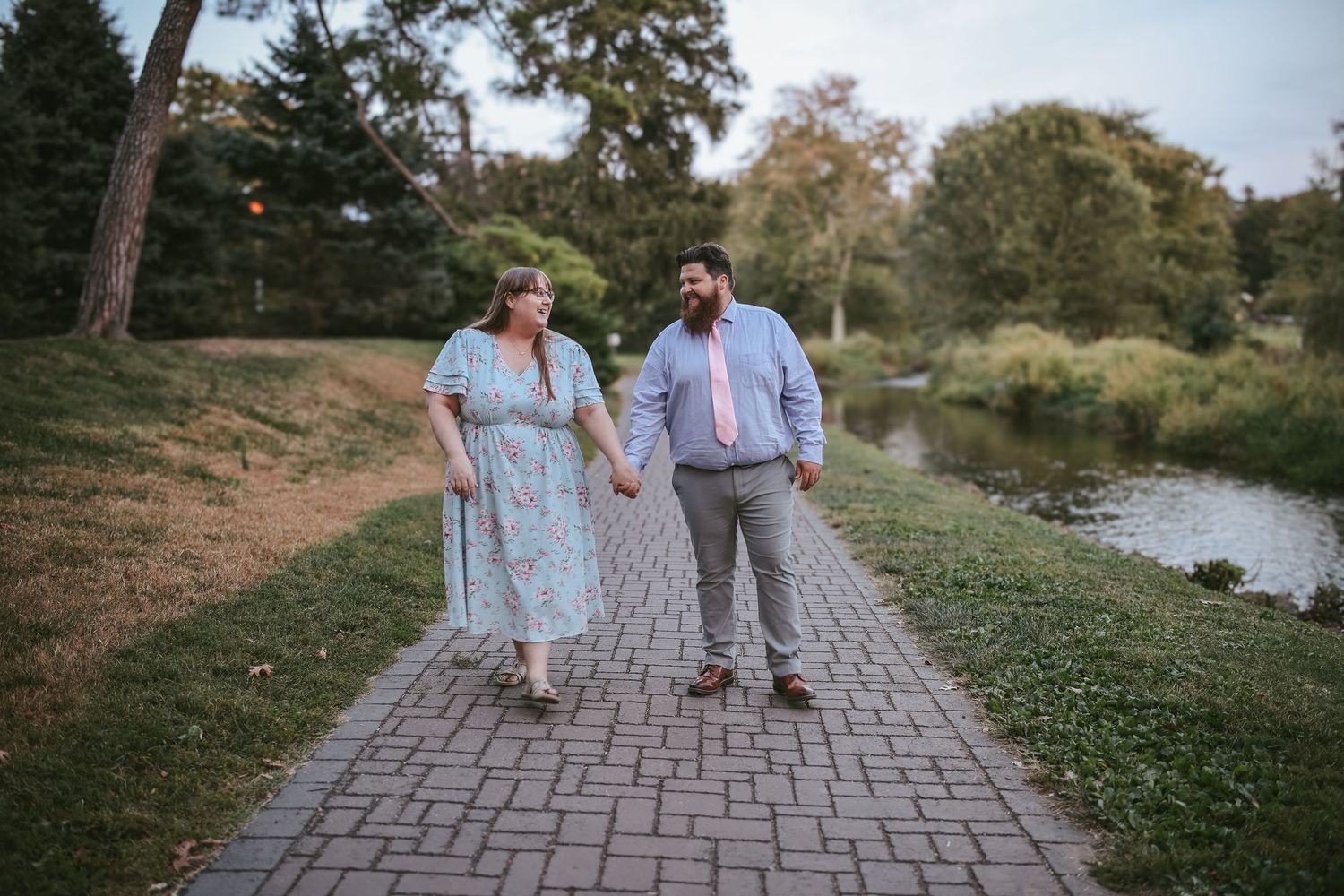 A couple walking together on a stone pathway through a scenic park during a sunny afternoon.