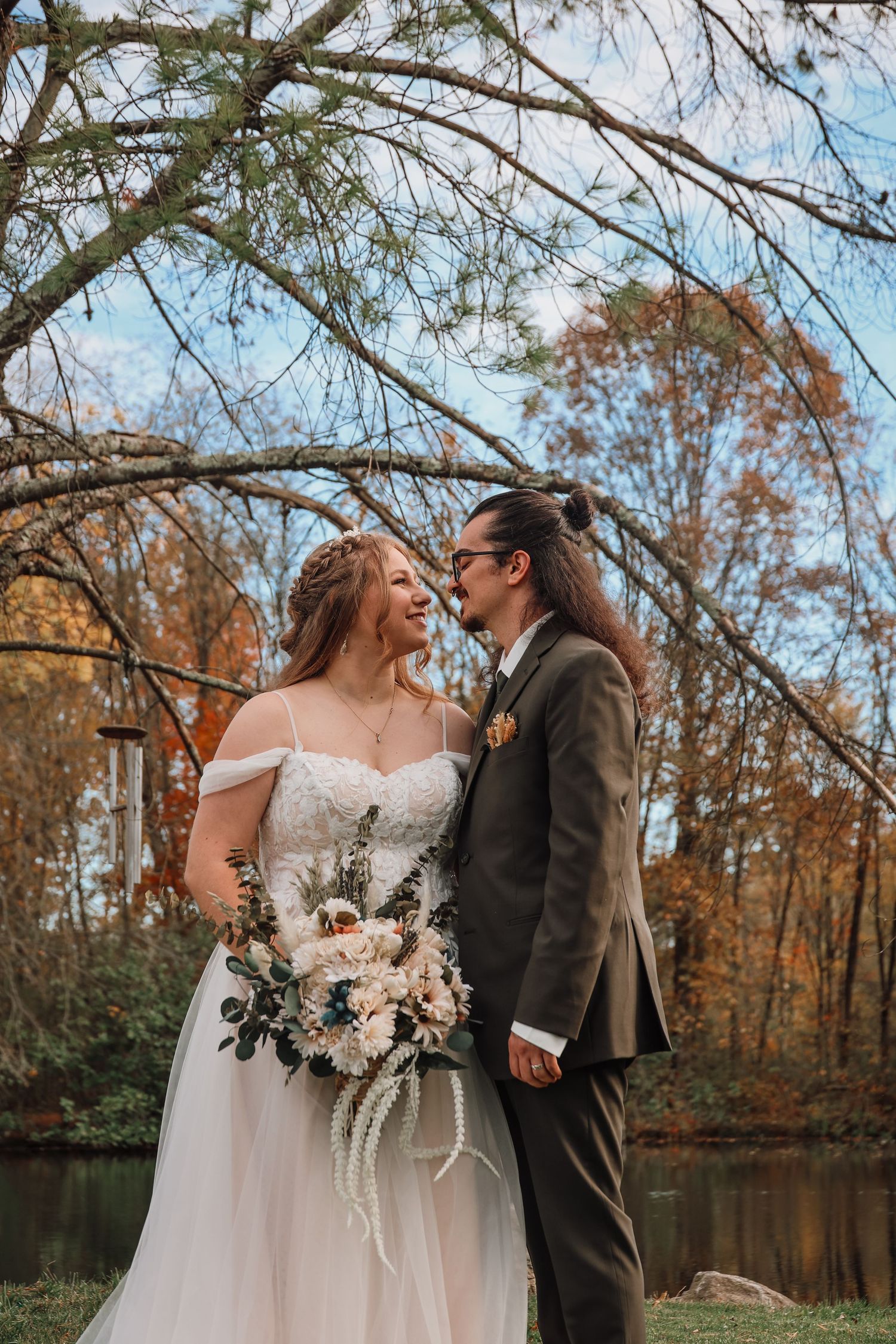 Wedding couple sharing intimate moment under autumn trees by lakeside.