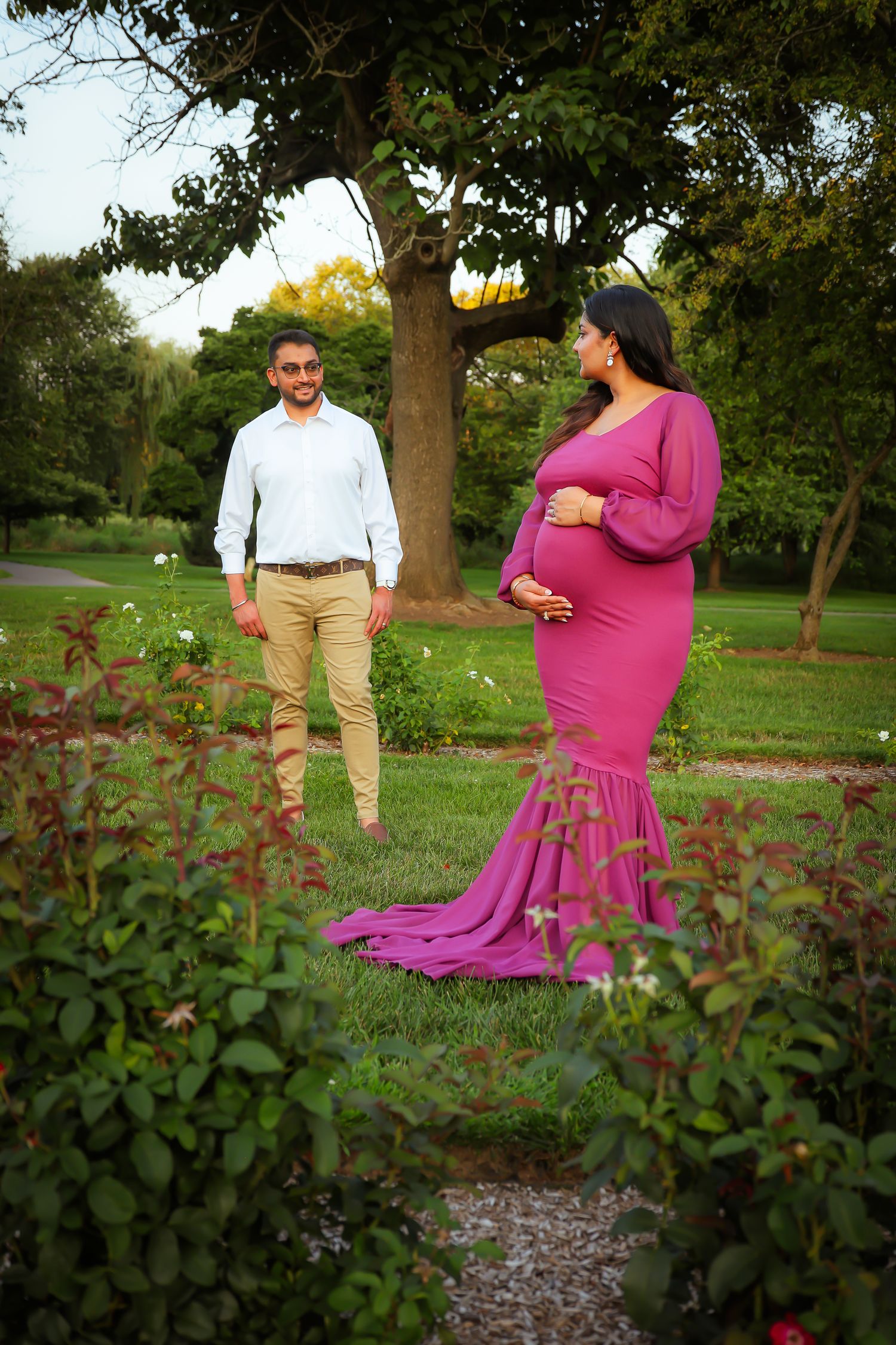 A couple poses together in a park setting with pink flowers in the foreground during a photo session.