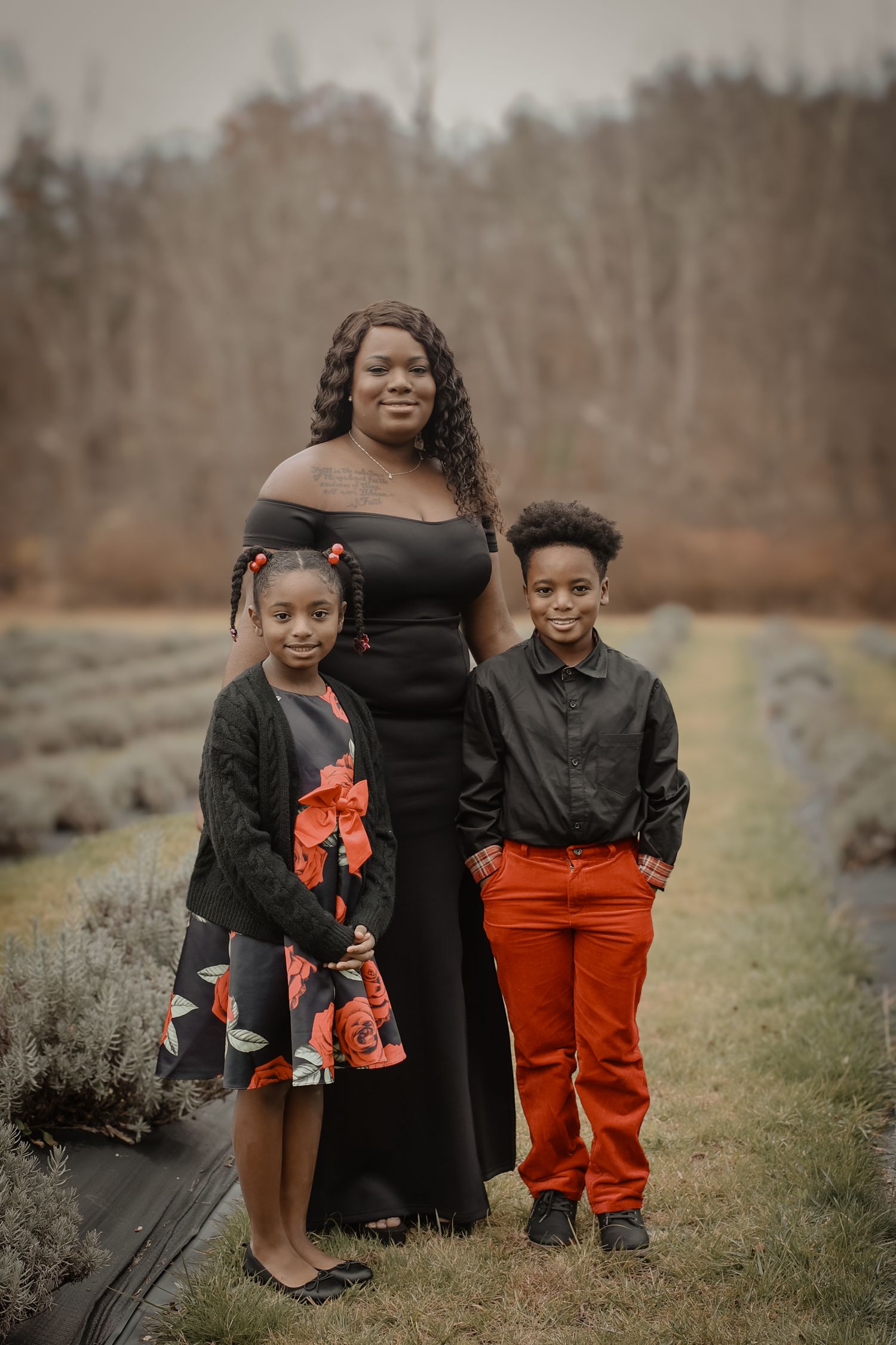 Family wearing coordinated black and orange outfits poses together outdoors in a natural setting during autumn.