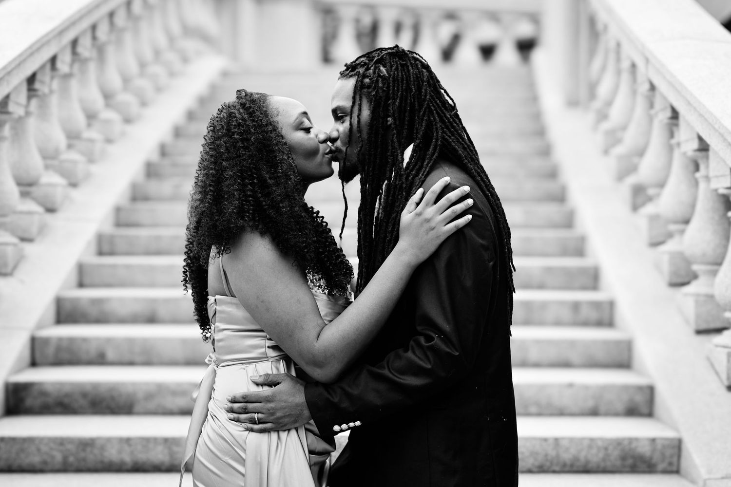 A romantic black and white portrait of a couple embracing on elegant white marble stairs.