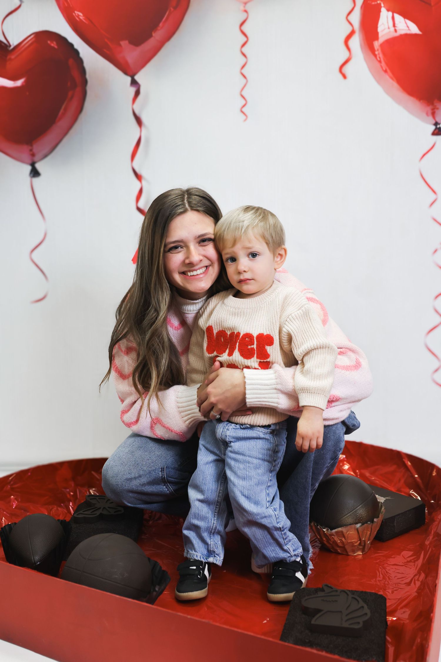 A Valentine's Day photo setup with red heart balloons and decorative elements against a white backdrop.