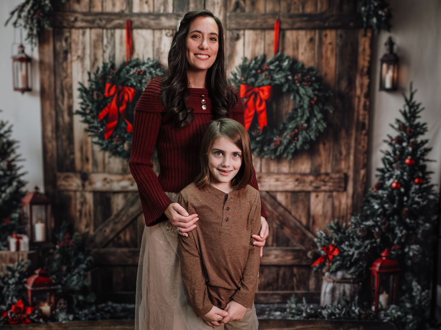 A festive holiday scene with people in warm winter outfits posing by rustic wooden doors with evergreen and red decor.