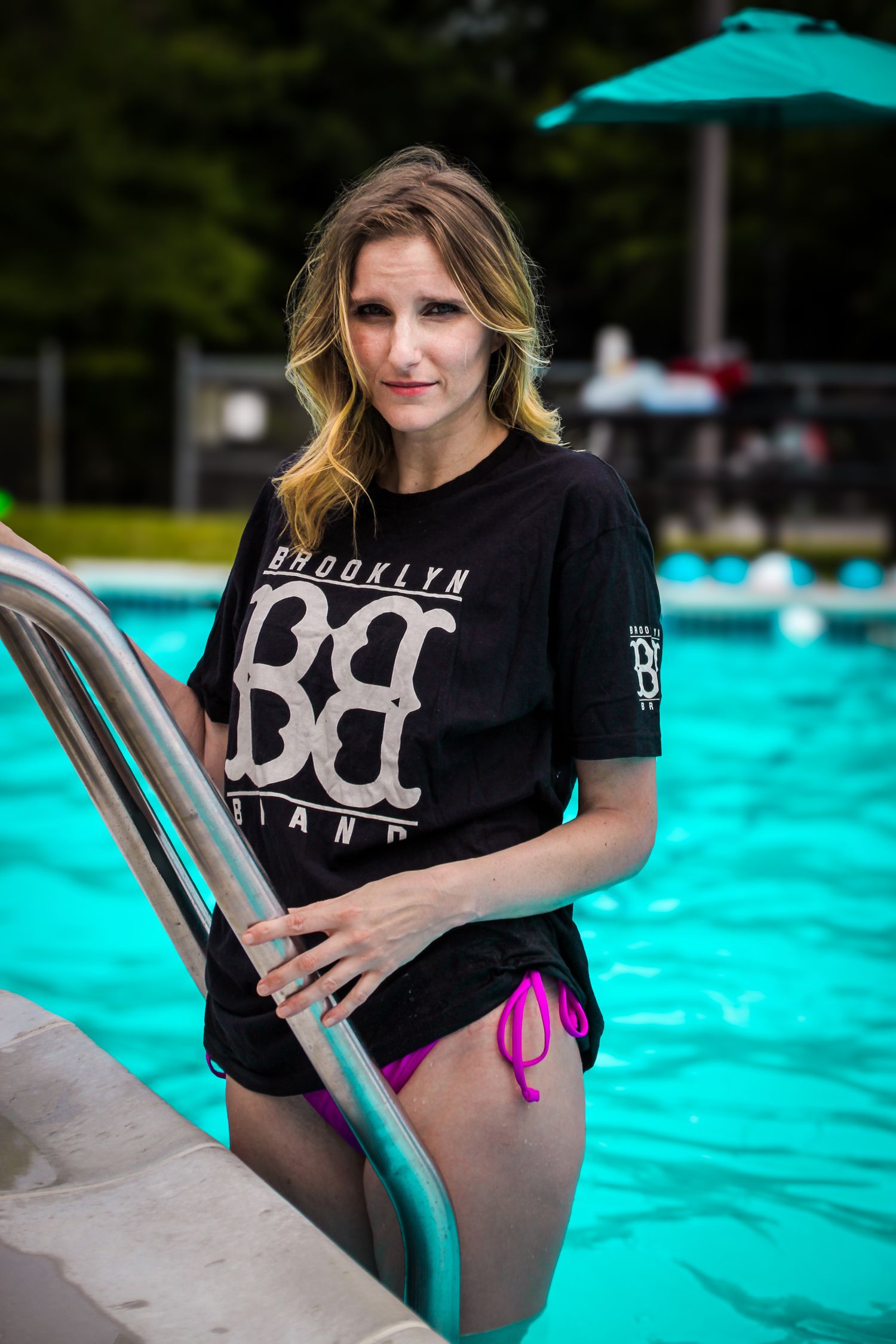 Person in black t-shirt poses by bright turquoise swimming pool on sunny summer day.