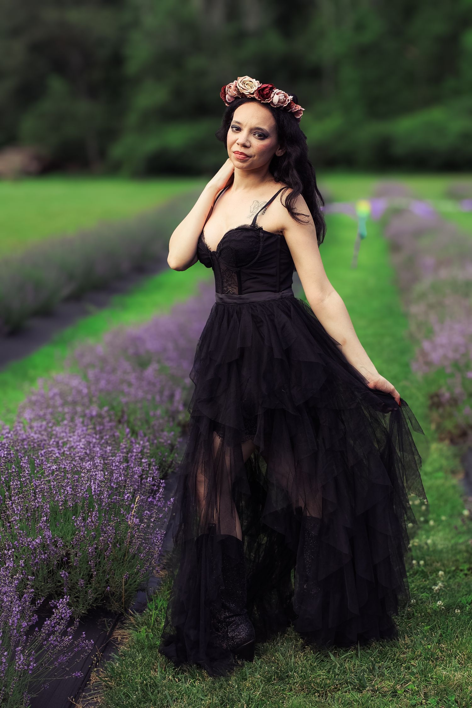 A person in a flowing black tulle gown poses gracefully in a garden with blooming purple lavender flowers.