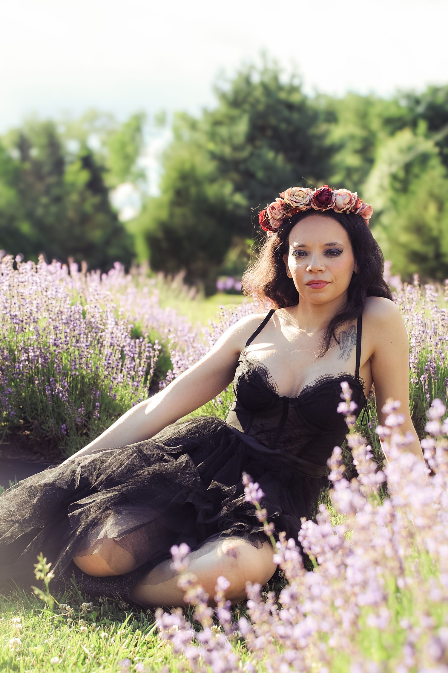A person wearing a floral crown reclines in a field of blooming purple lavender flowers on a sunny summer day.