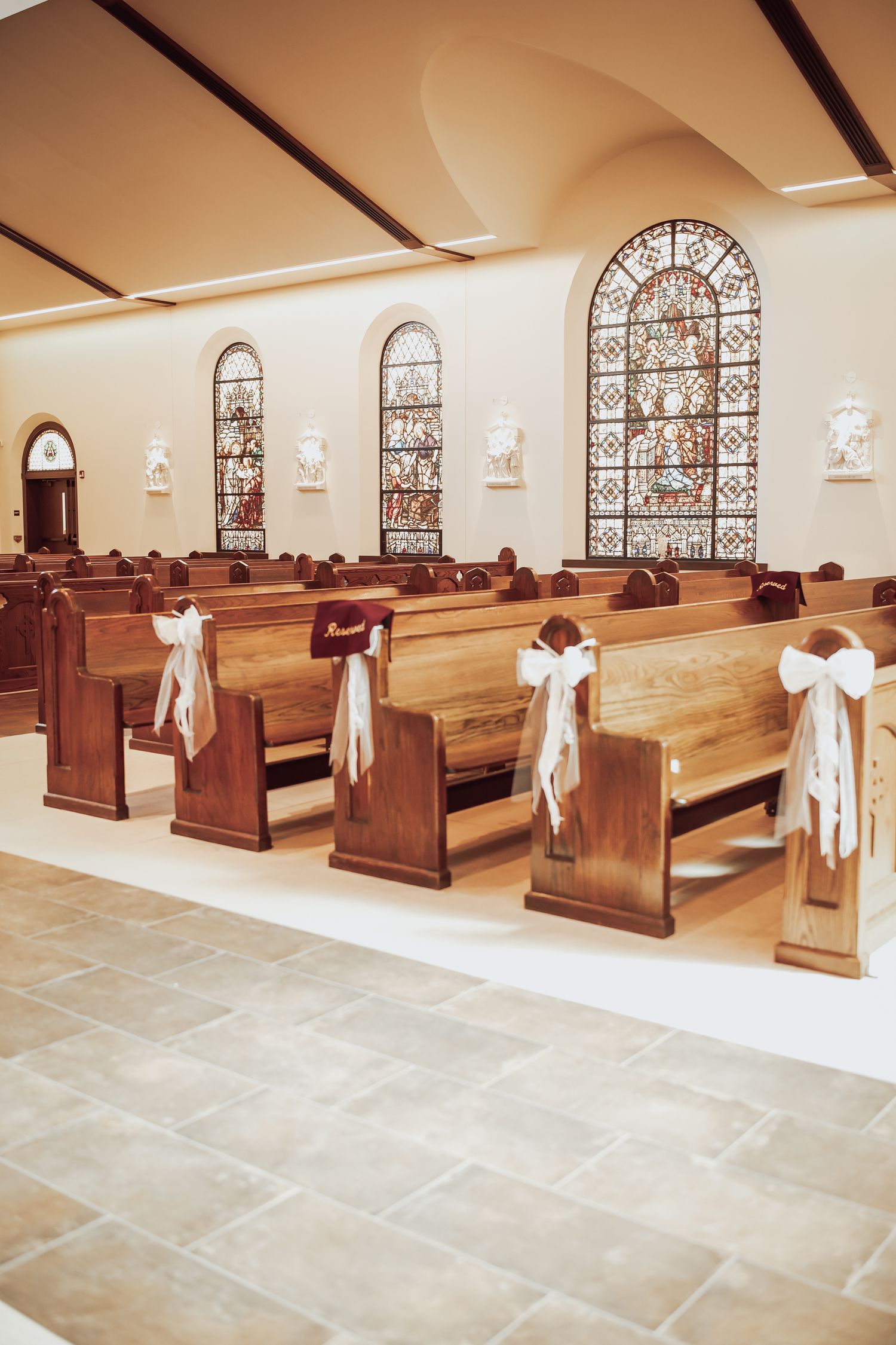 Church interior with wooden pews, stained glass windows, and white decorative bows adorning the aisle seating.