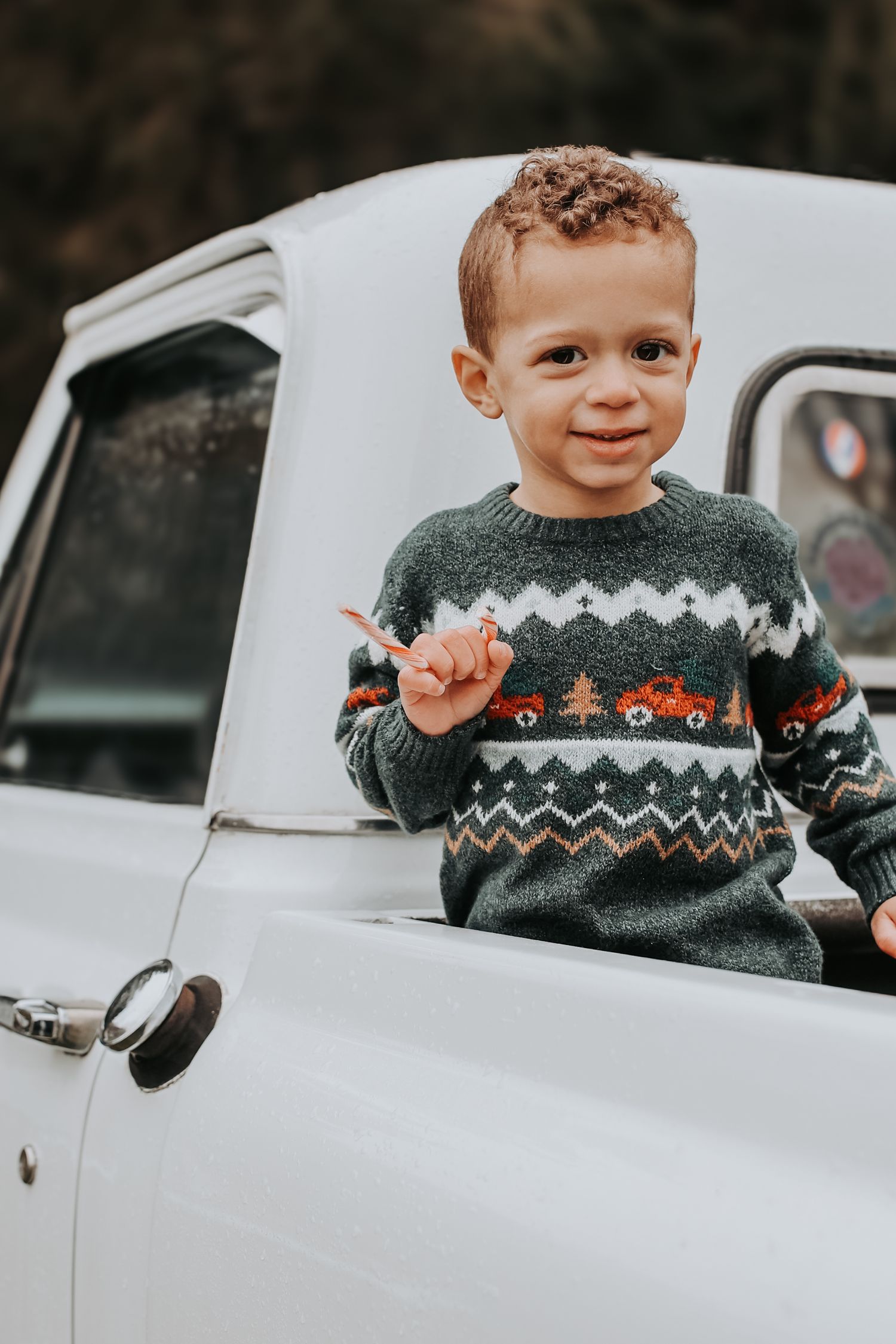 Child wearing a festive holiday sweater with zigzag pattern peeks out of a white vintage car window.