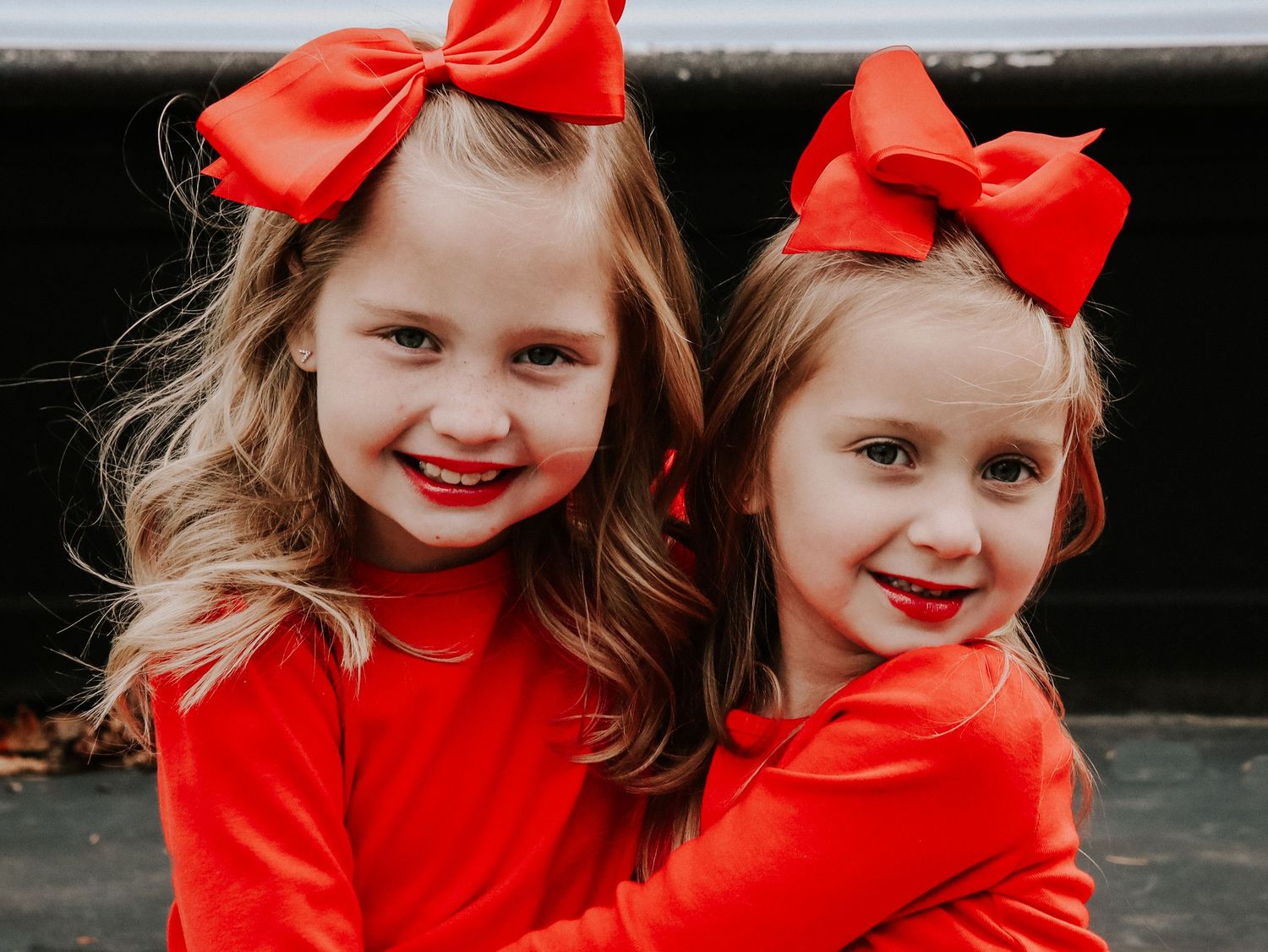 Children wearing matching bright red outfits and bows smile while playing together outdoors.