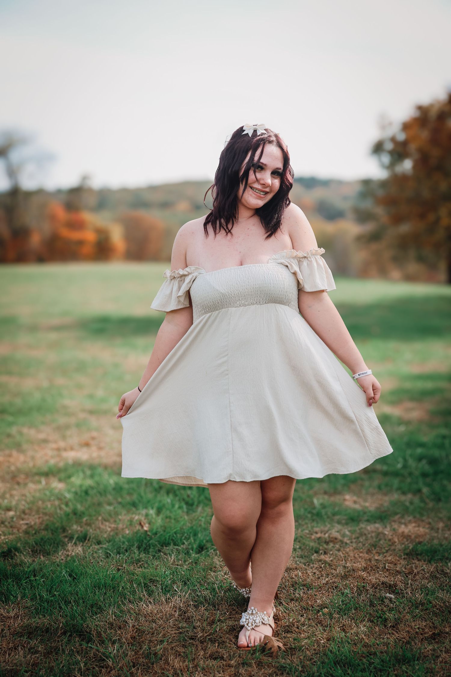 A person in a white dress twirls playfully in a grassy field during autumn.