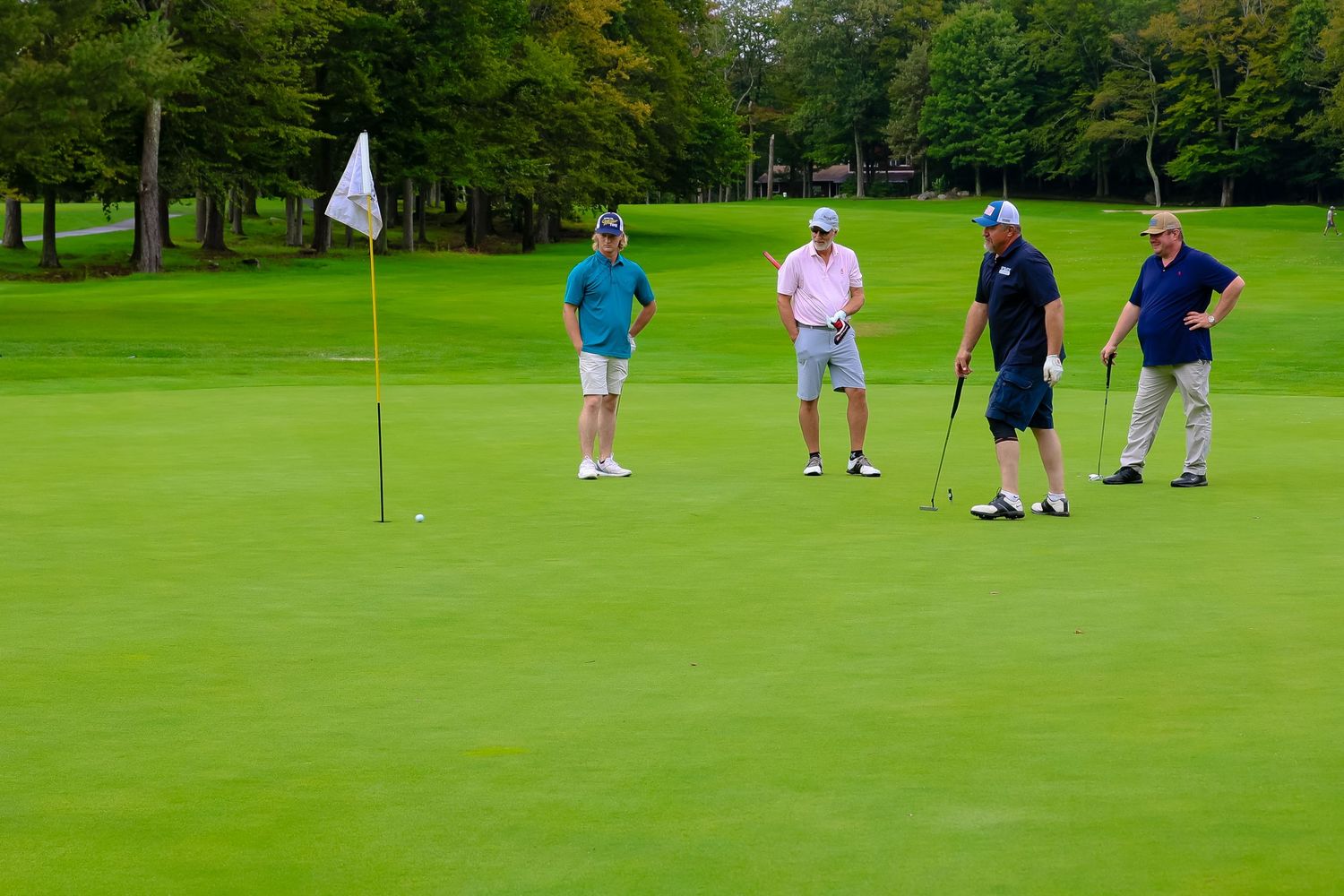 Golfers practicing their putting skills on a lush green golf course during a sunny day.