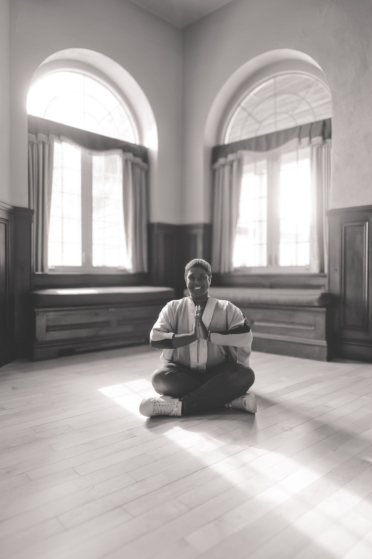 A person sits cross-legged reading a book in a bright minimalist room with arched windows and natural light.