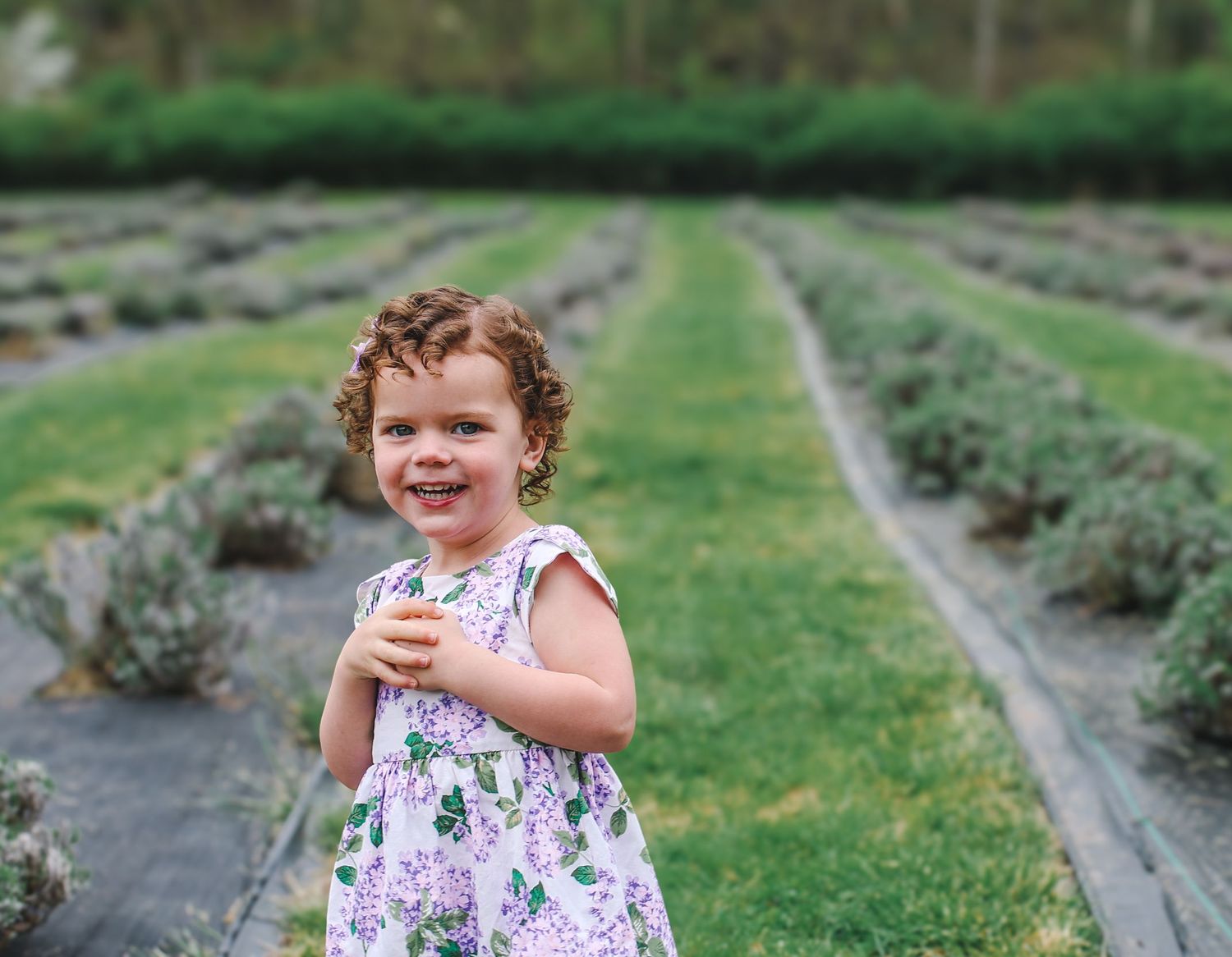 A young child in a floral dress laughs while running through garden rows at a farm.