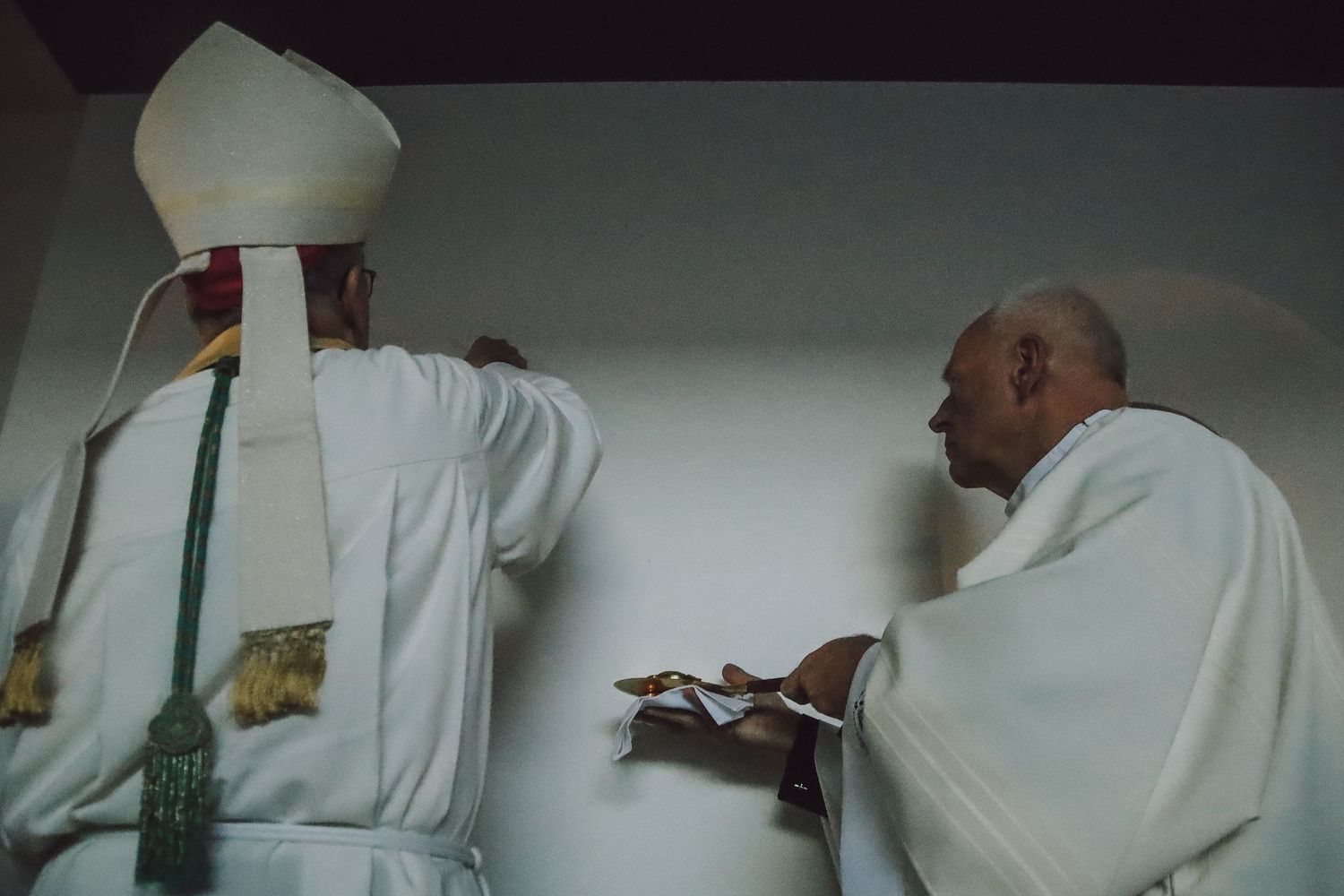 Two clergy members in white robes stand at the altar during a religious service.