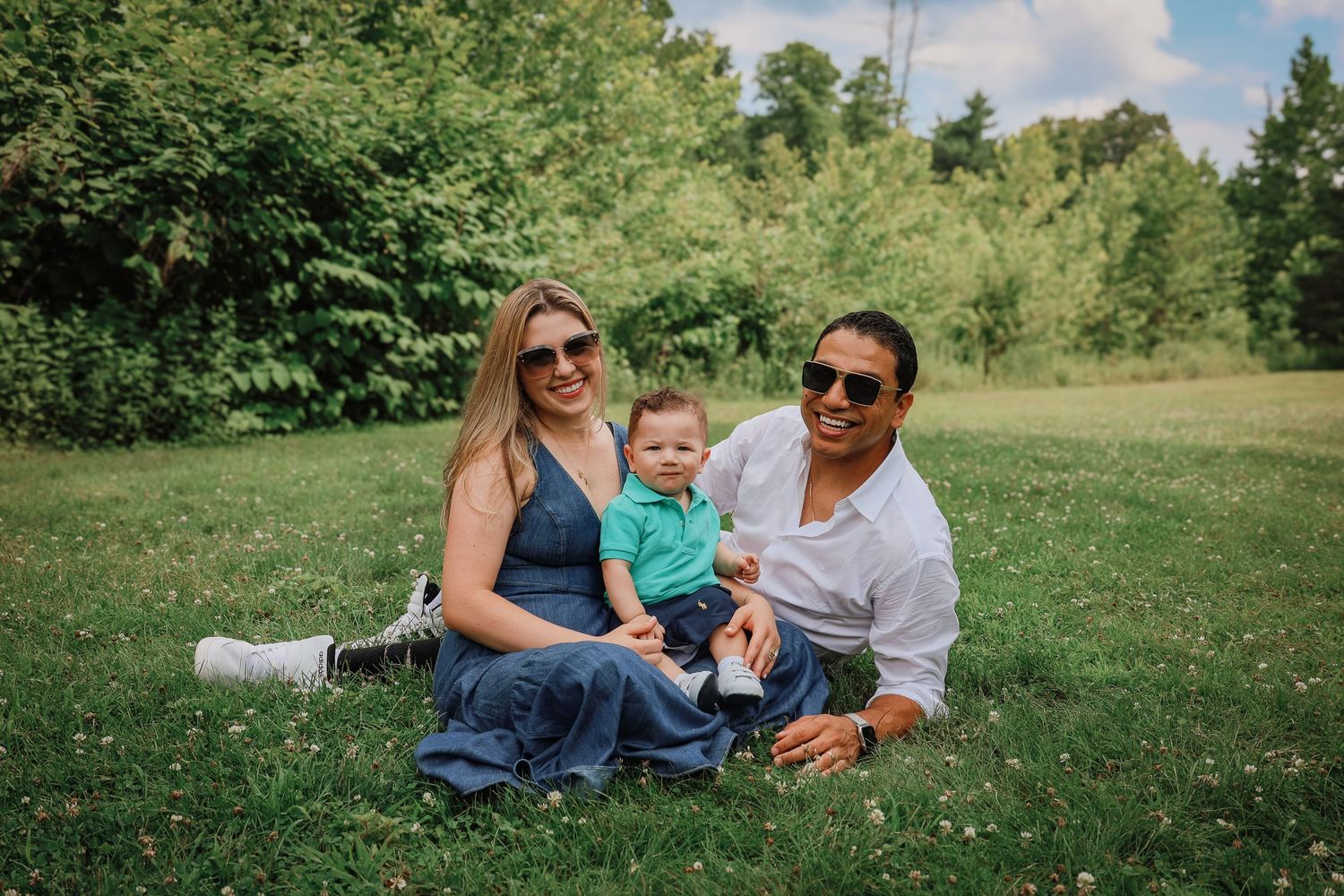 A family relaxes together on green grass during a sunny summer day in a park setting.