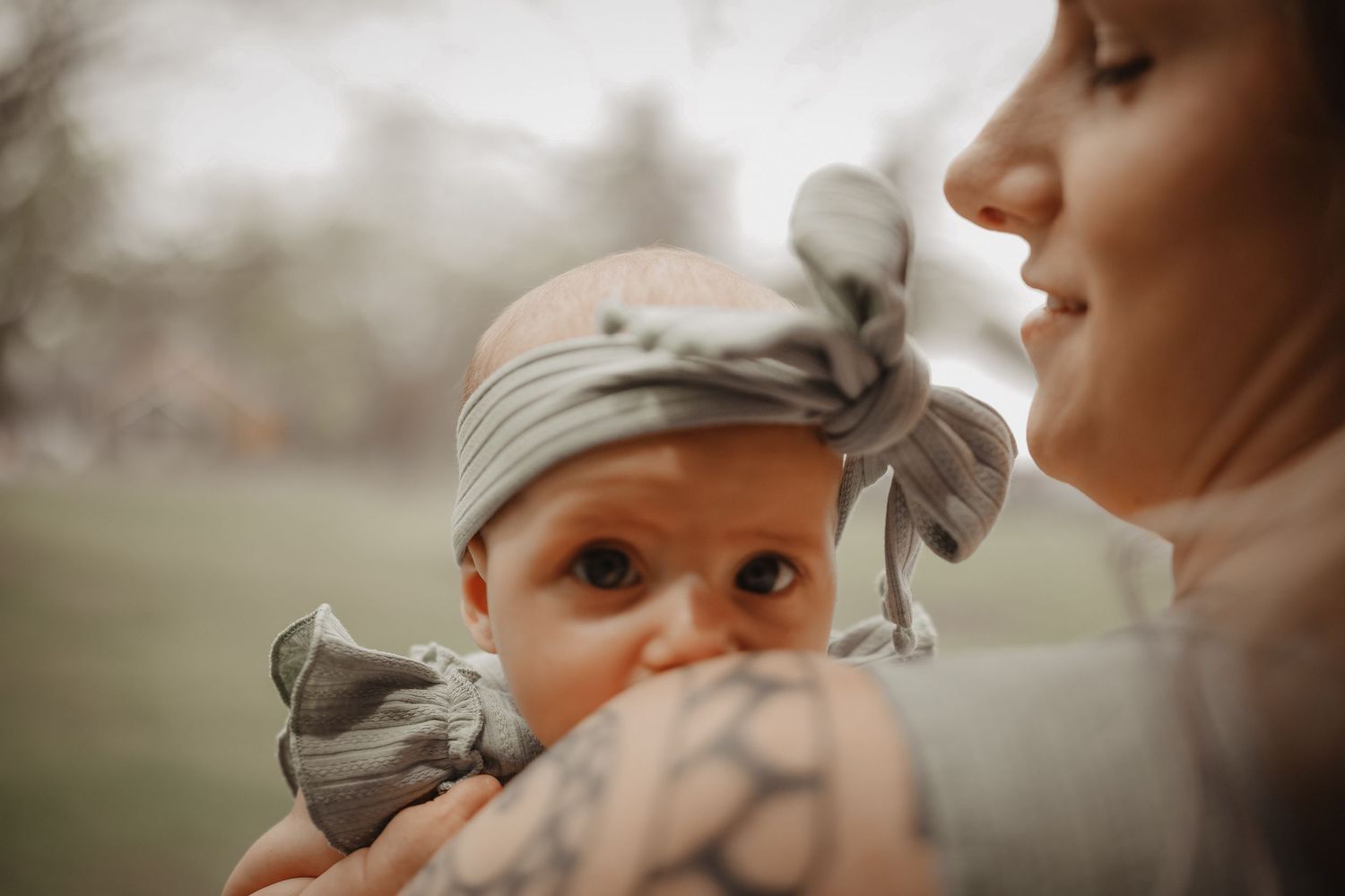 A baby in a gray hat gazes lovingly at their caregiver in a tender moment captured in soft lighting.