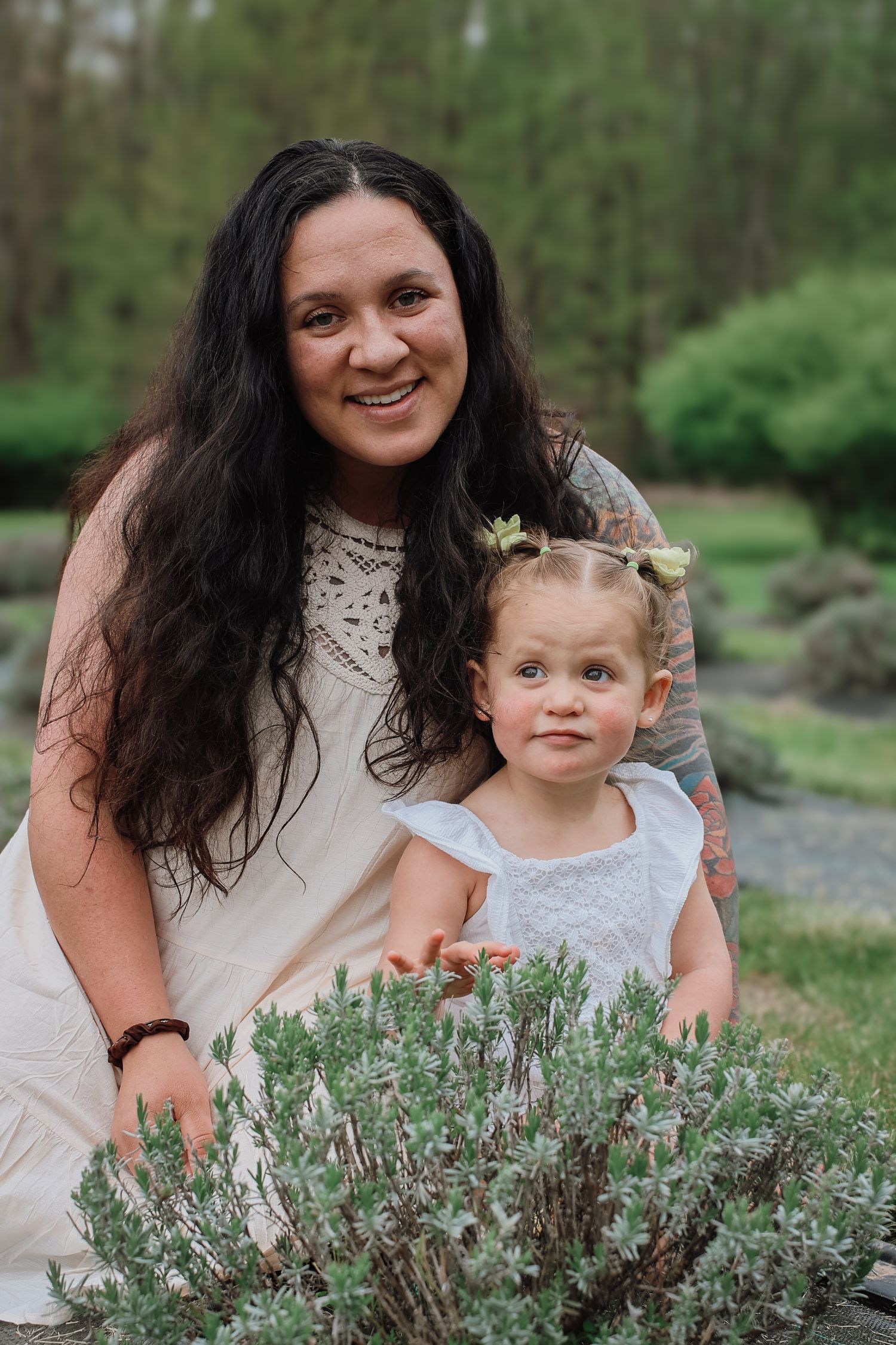 A parent and toddler in white dresses pose together in a garden setting with lavender plants in the foreground.