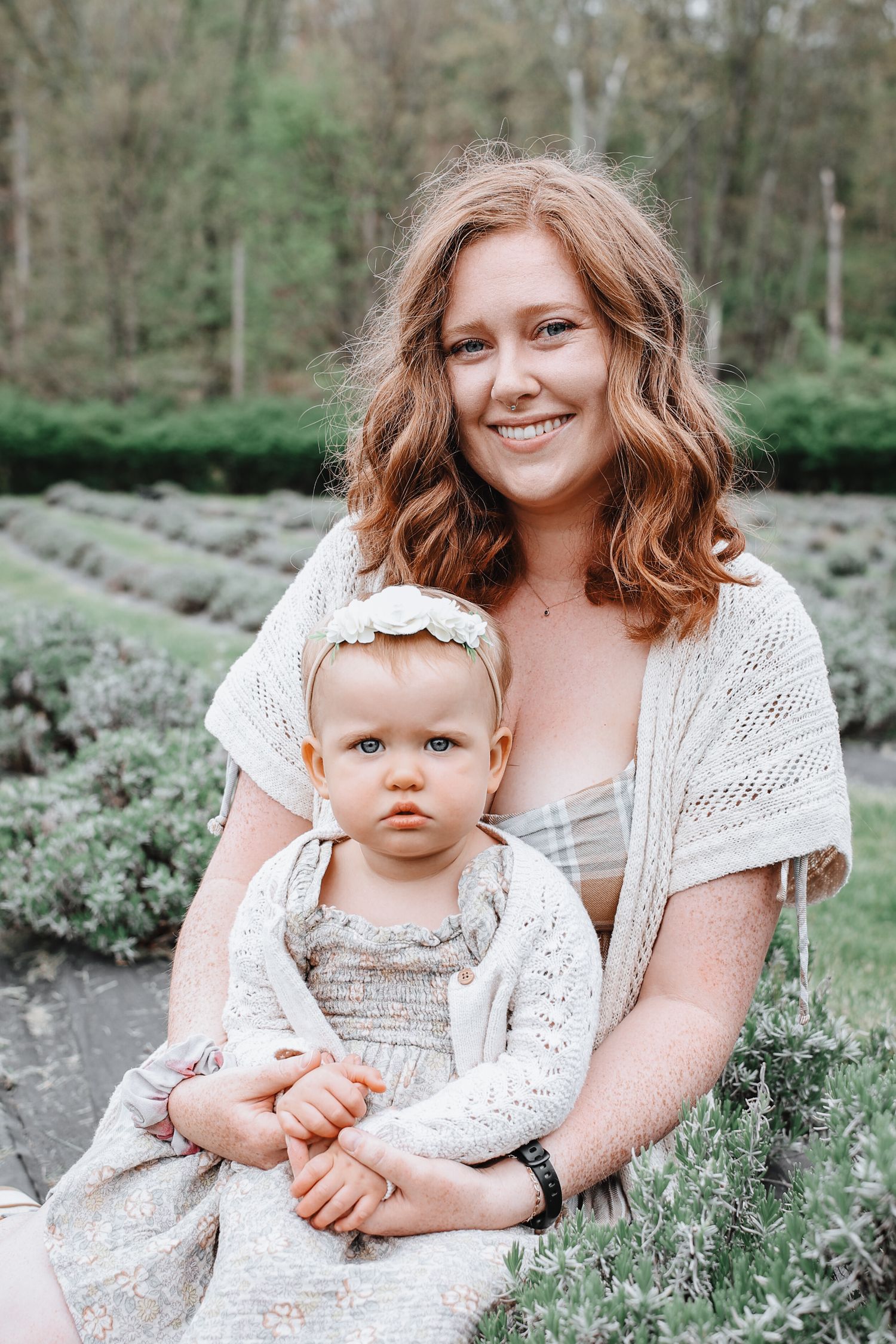 A parent and baby sit together in a field of white wildflowers wearing matching light-colored outfits.