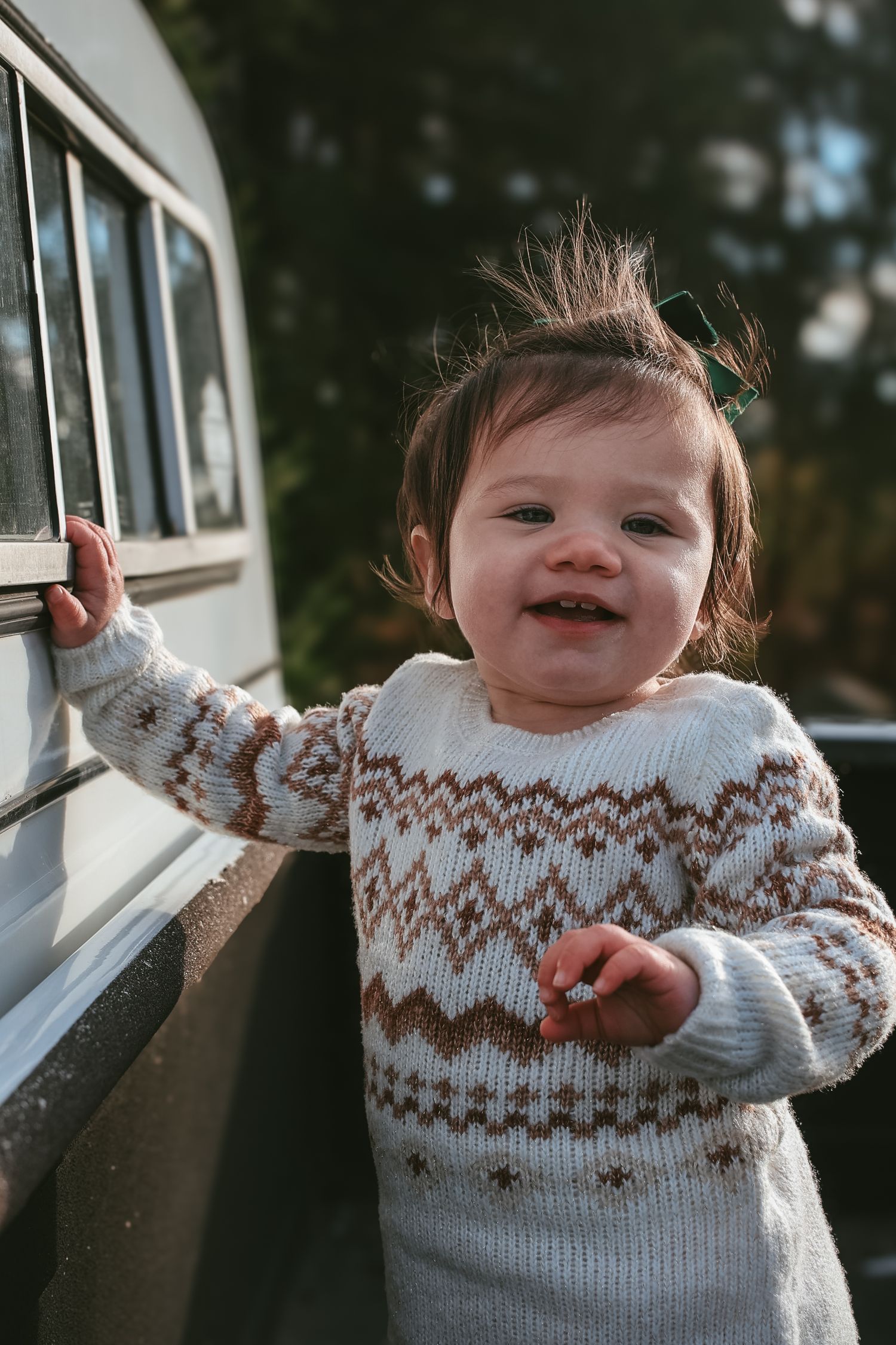 A small child wearing a white and brown patterned knit sweater plays near a window in a sequence of candid shots.