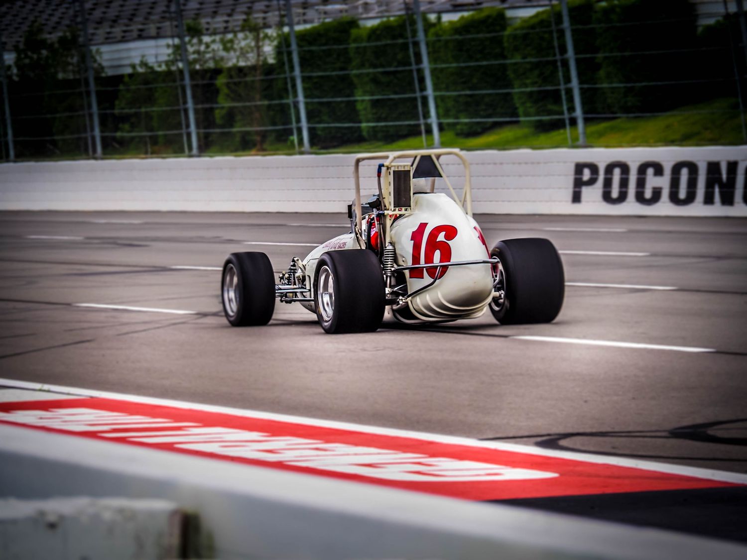 A race car speeds around a corner at the Pocono Raceway during a competitive motorsport event.