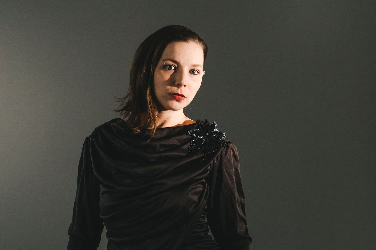 Woman in black draped top with red lips poses against gray background in professional portrait photo.