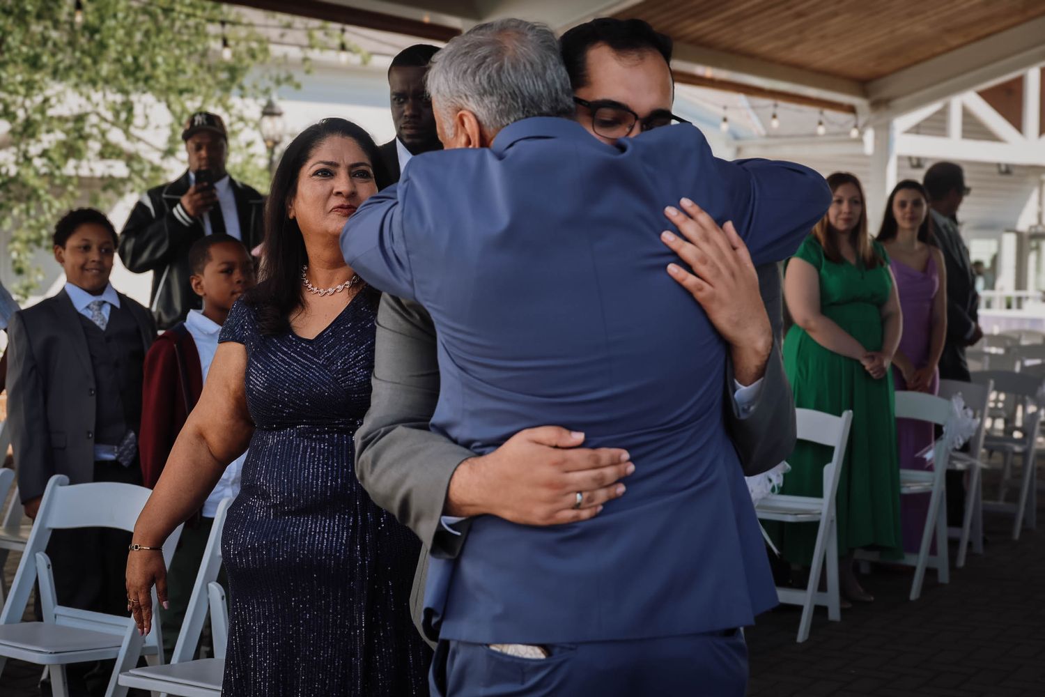 Groom shares an emotional hug with a guest during an outdoor wedding ceremony.