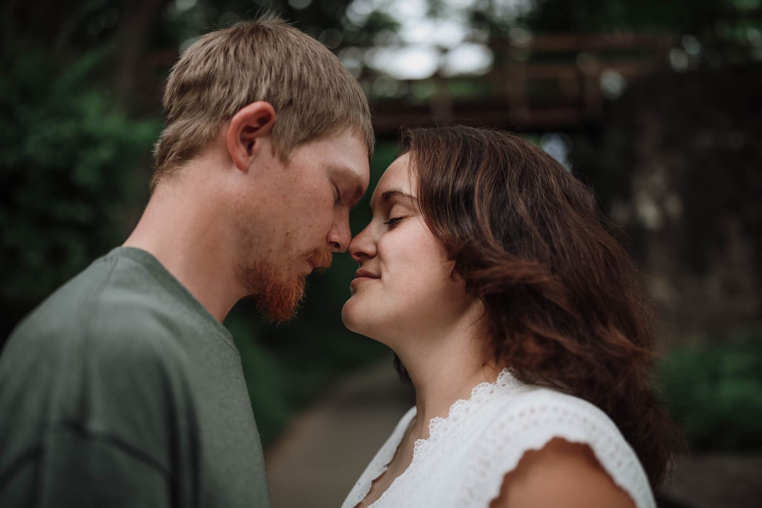 Romantic couple leaning in for a kiss outdoors in a lush green setting.