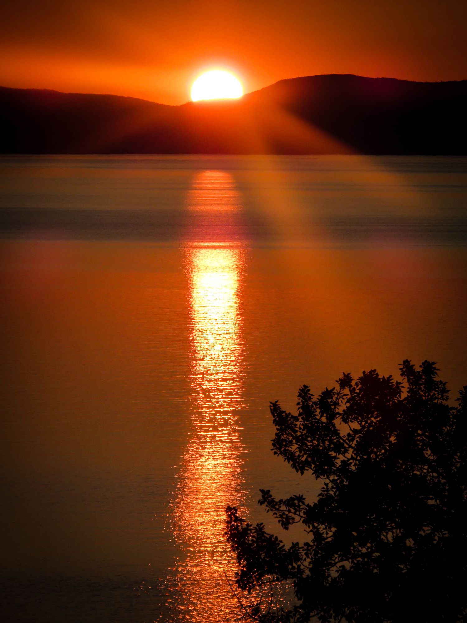 Golden sun setting between mountains creates a glowing reflection path on dark waters.
