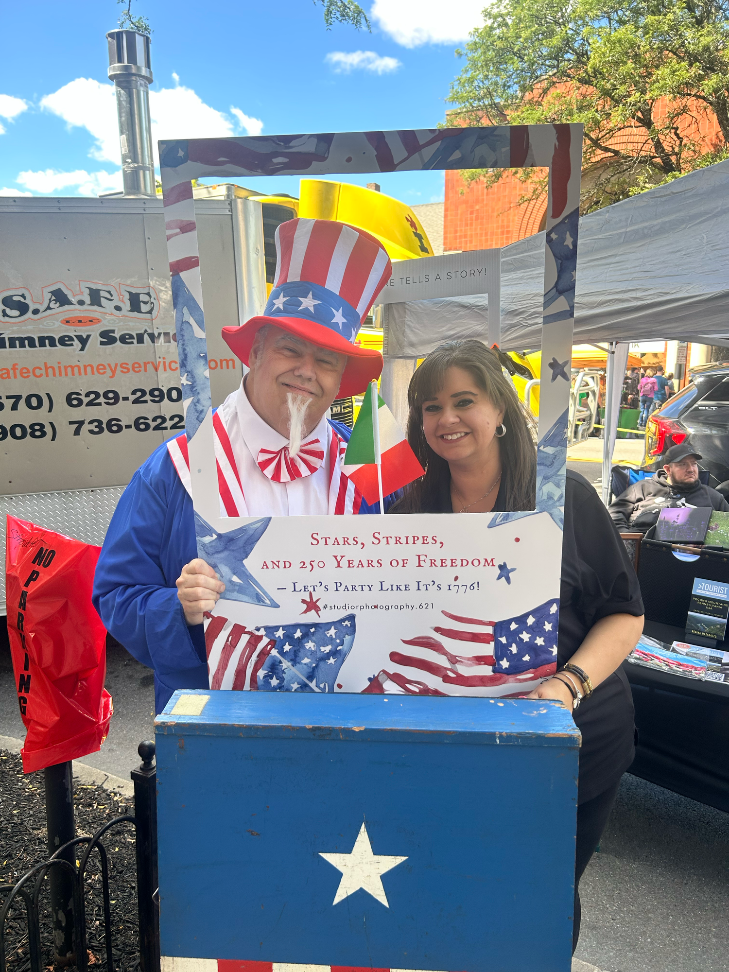 Patriotic scene at outdoor event with American flag decorations and star-adorned display booth against blue sky background.
