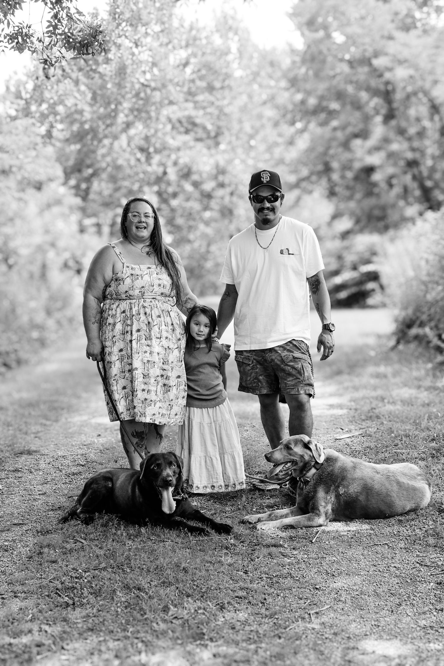 Family and their dogs relaxing together on a grassy hill in black and white photography.