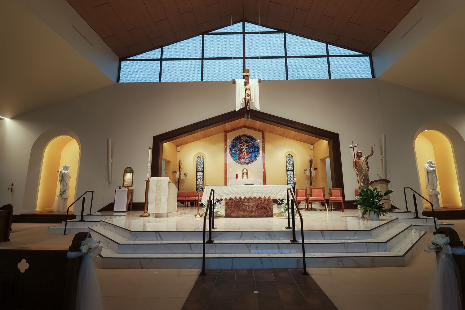 Interior view of a modern Catholic church sanctuary with large triangular window and raised altar platform.