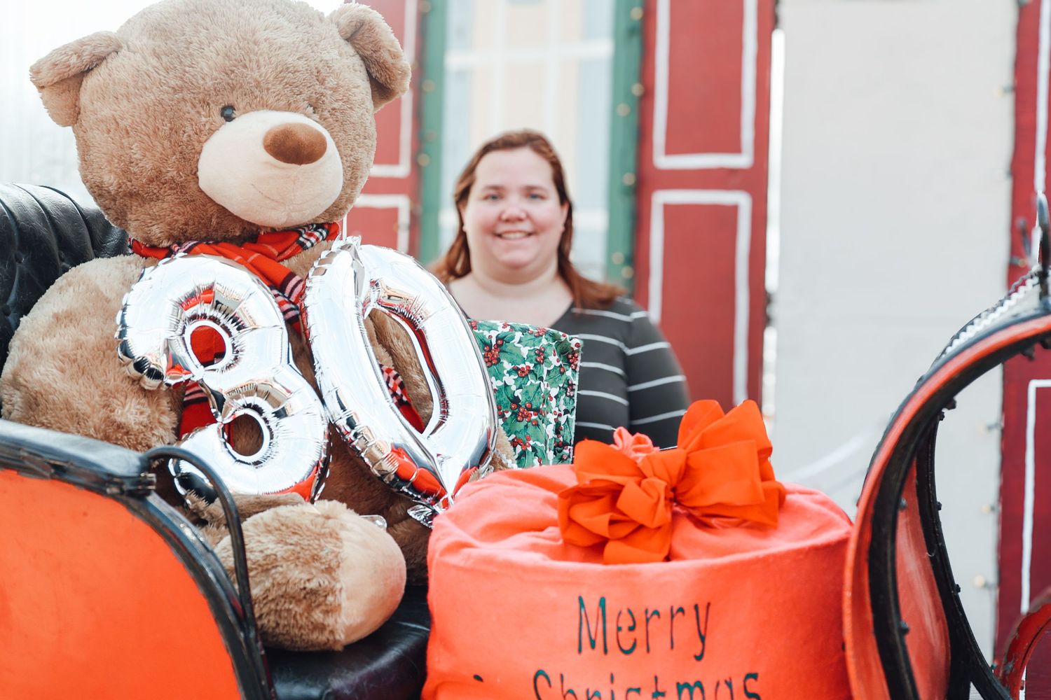 A collection of stuffed teddy bears arranged in orange baskets with Christmas decorations against a red wall.