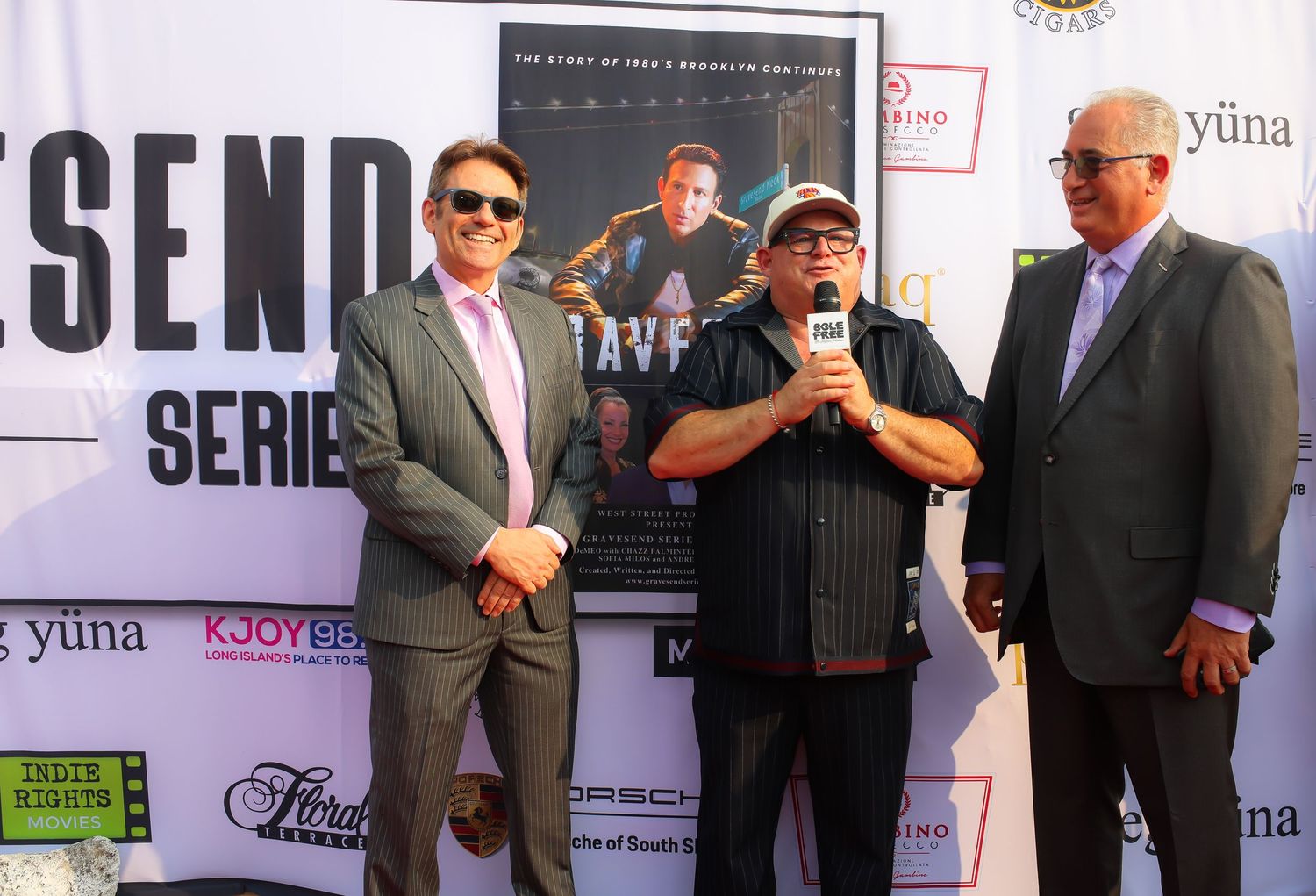 A group of people in formal attire standing against a backdrop with promotional banners and signage at an event.