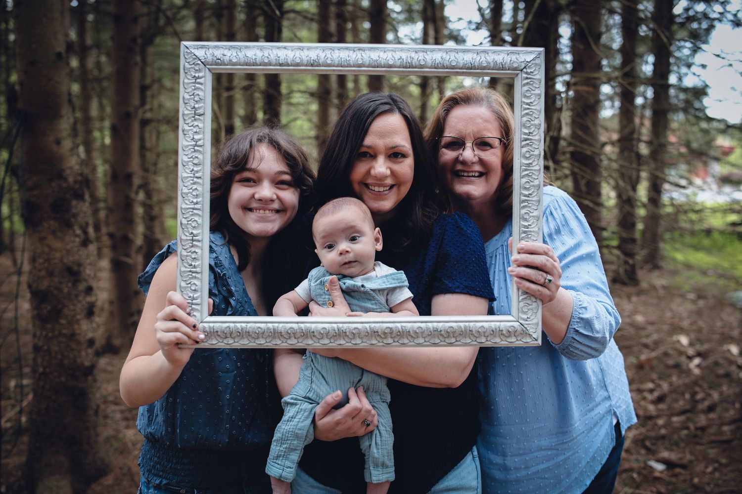 A group poses together outdoors in a forest setting holding a blue frame prop for a creative photo shoot.