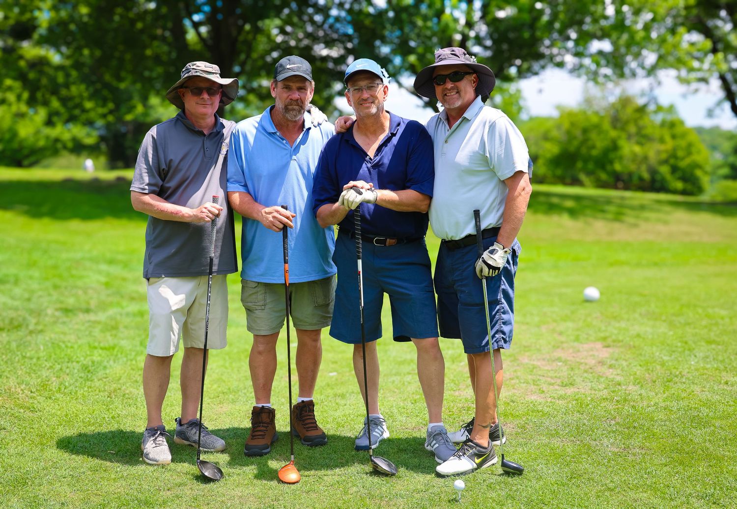 Group of senior golfers standing together with clubs on a sunny green golf course.