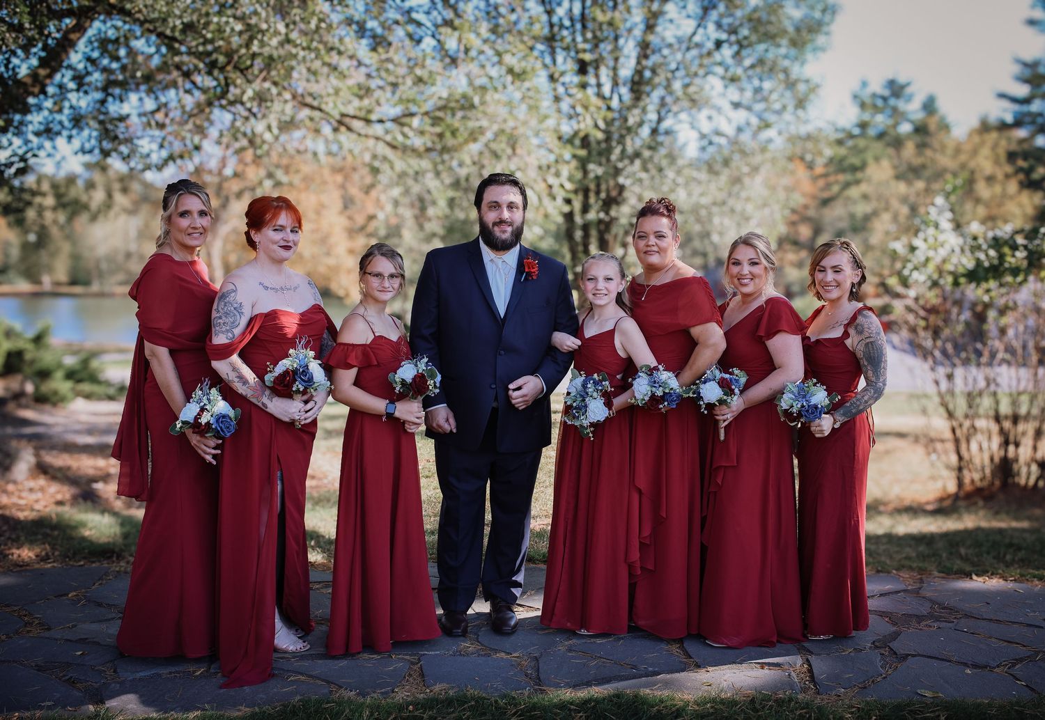 Wedding party in burgundy dresses and dark suits poses together outdoors on an autumn day.