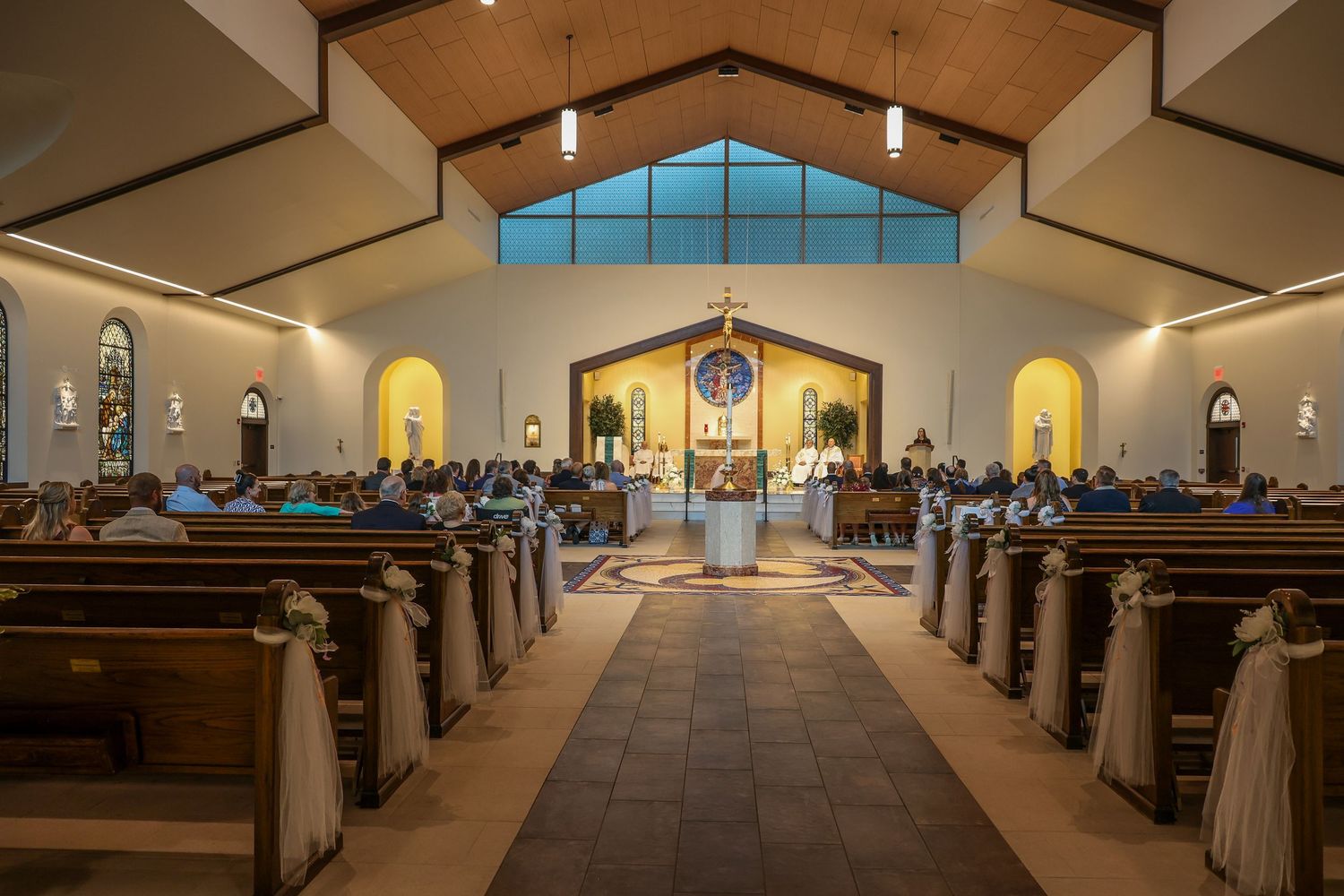 Panoramic interior view of a modern Catholic church sanctuary with wooden pews and altar illuminated by natural light.