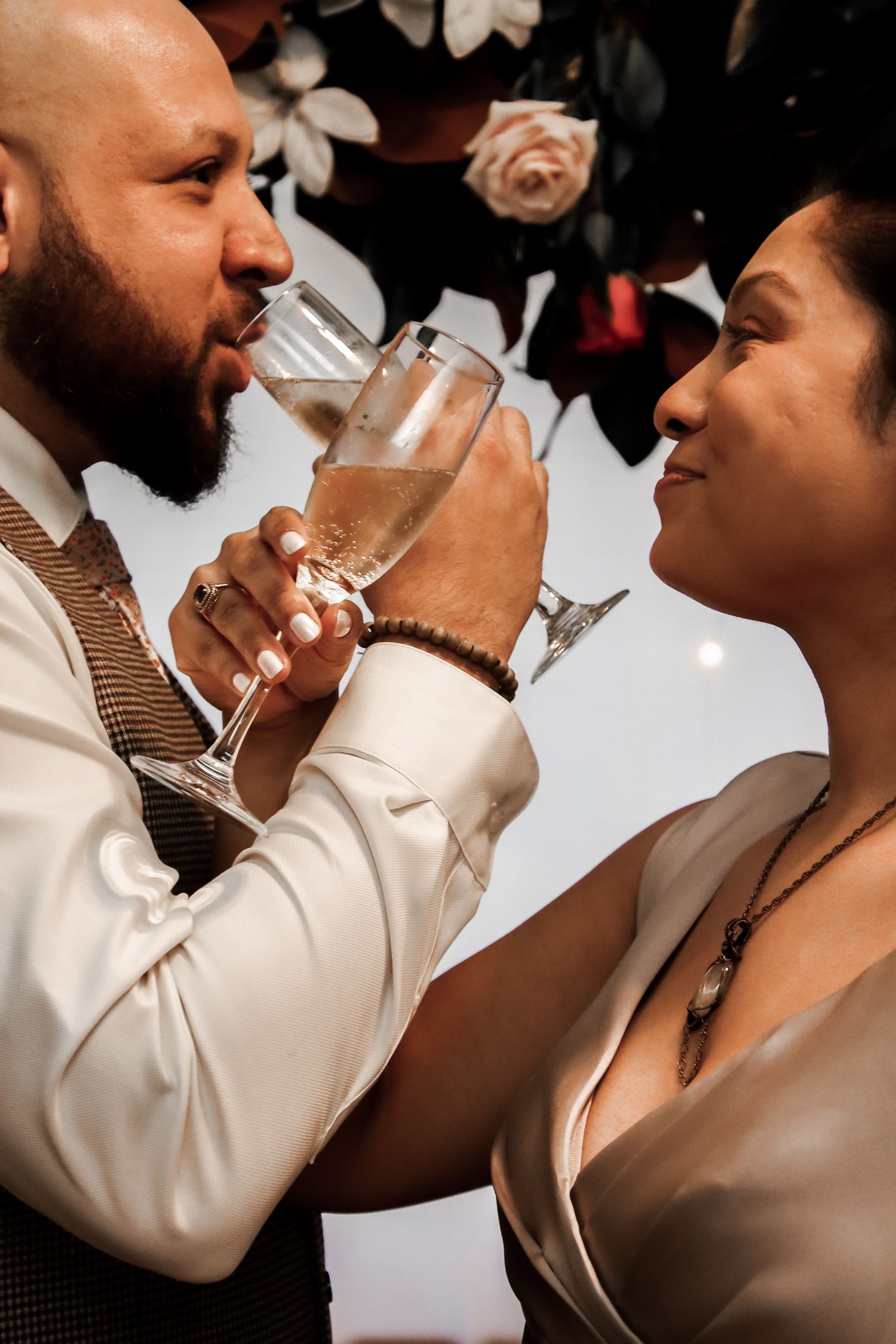 A romantic couple shares champagne glasses while gazing at each other during an elegant celebration.